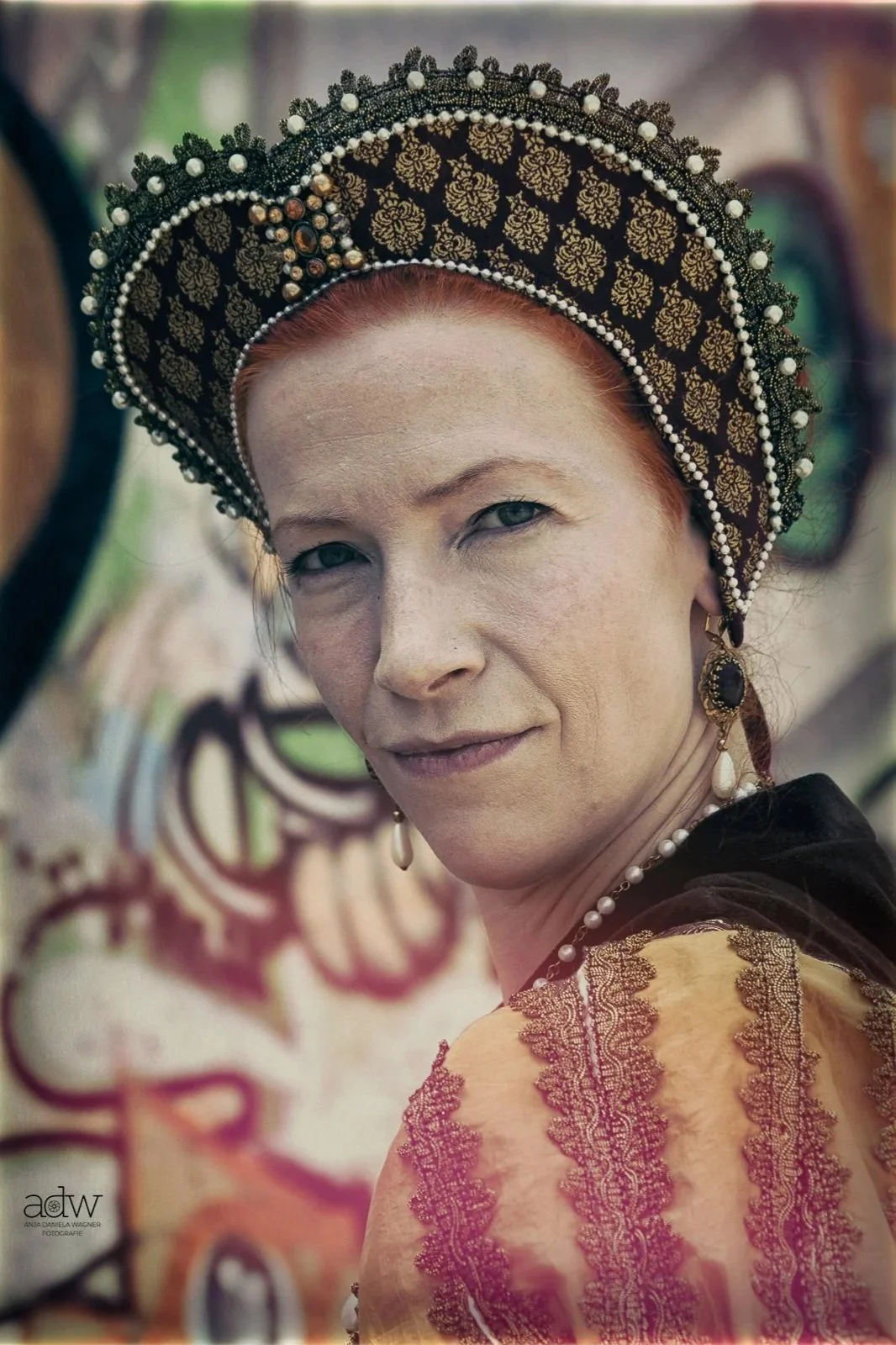 A woman with red hair wearing a traditional ornate headdress, earrings, and a colorful embroidered garment.
