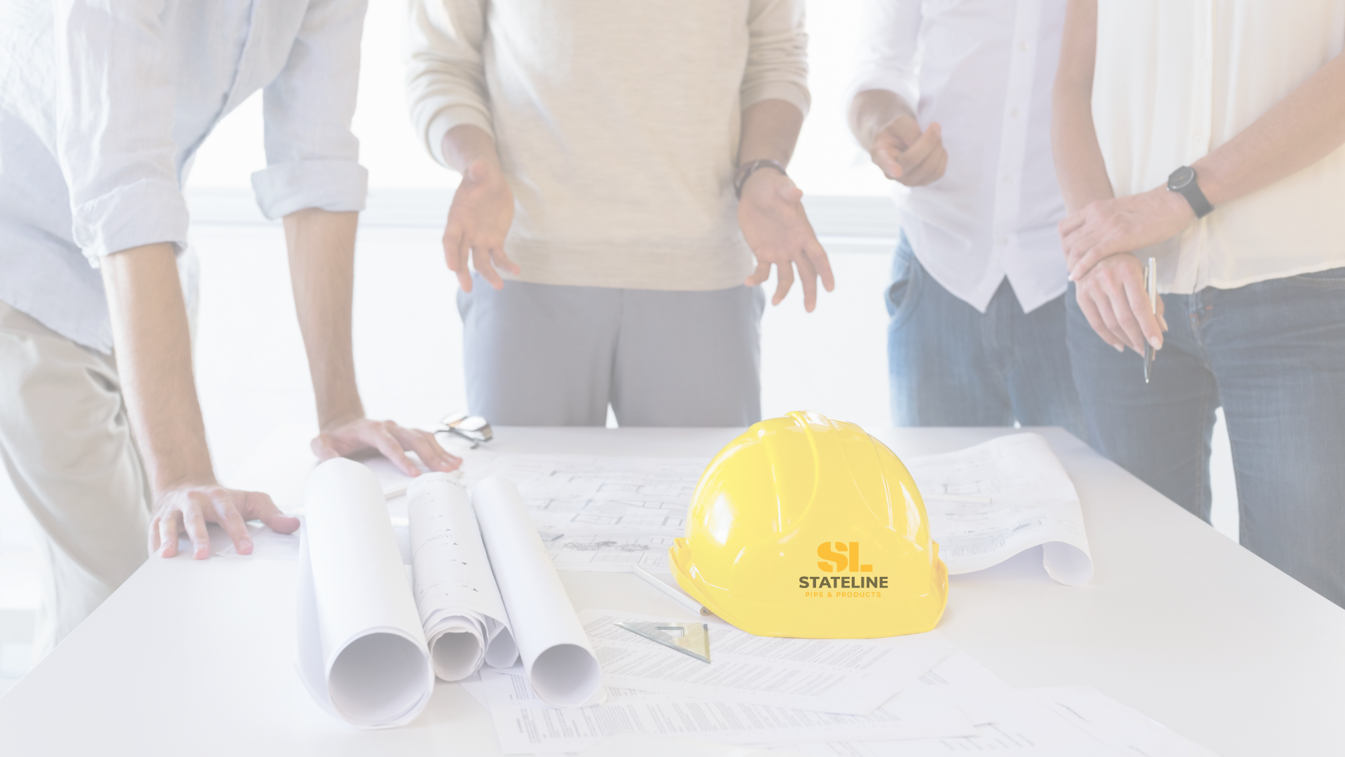 Four people gathered around a table with blueprints and a yellow hard hat with the SL Stateline logo.