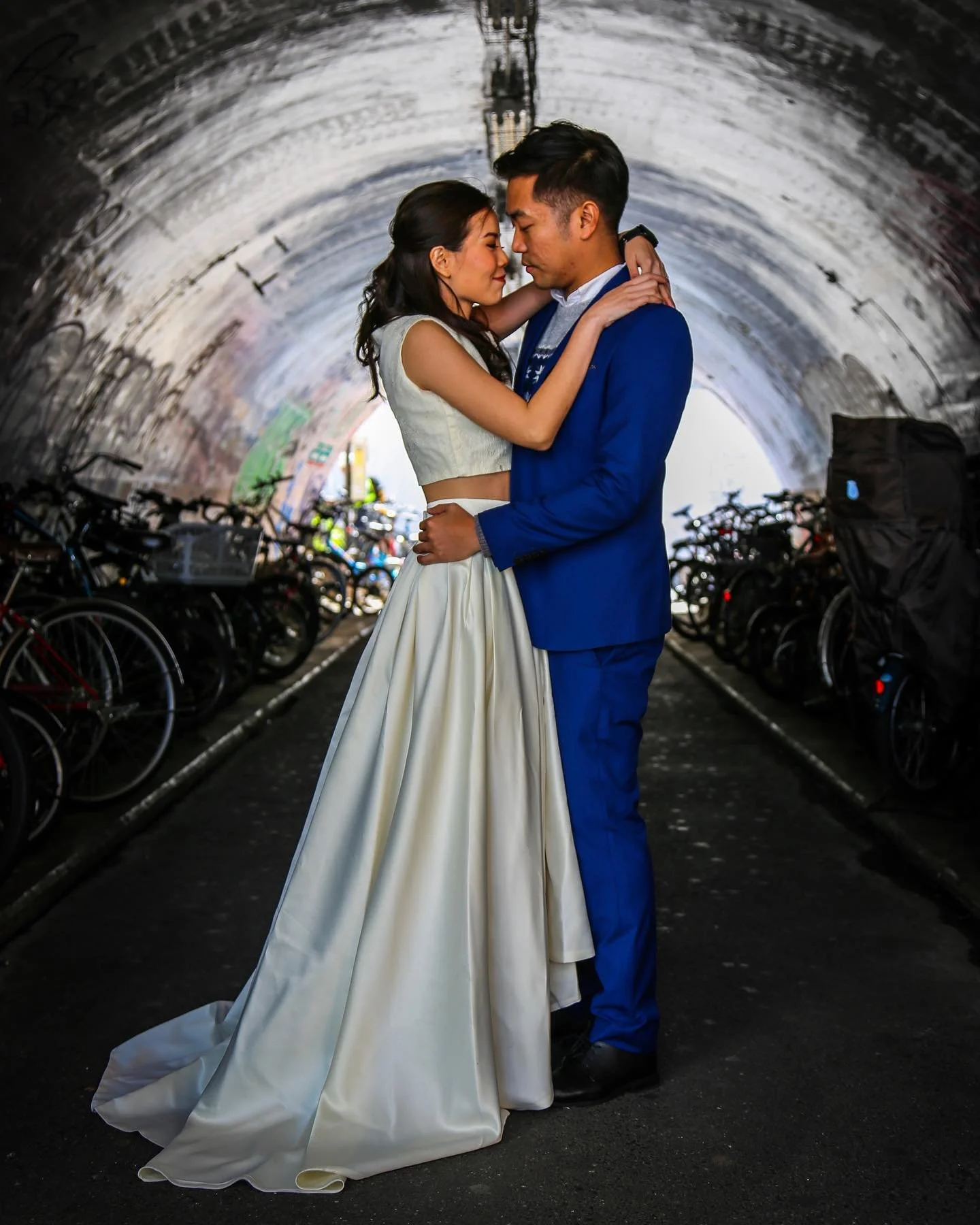 A couple dressed in wedding attire sharing an intimate moment in a tunnel, with bicycles parked along the sides.
