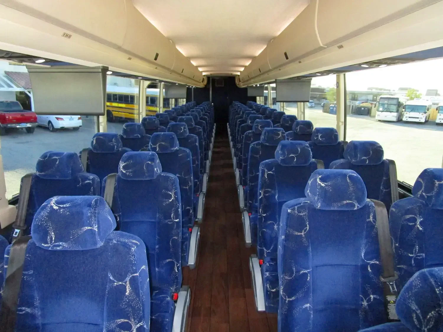 Interior of a bus with multiple blue fabric seats, a central aisle, and large windows on both sides showing parked buses and vehicles outside.