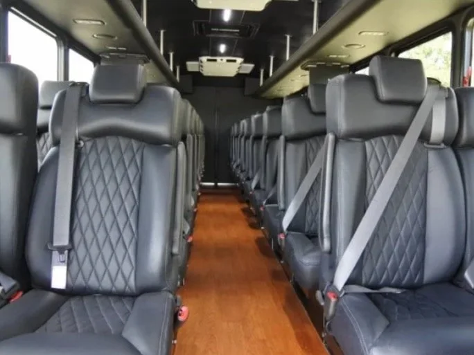 Interior of a Freightliner mini-bus with black leather seats arranged in rows, with seatbelts fastened and a wood floor.