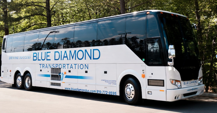 Blue and white Blue Diamond Transportation Prevost Motor Coach parked on a road, with trees in the background.