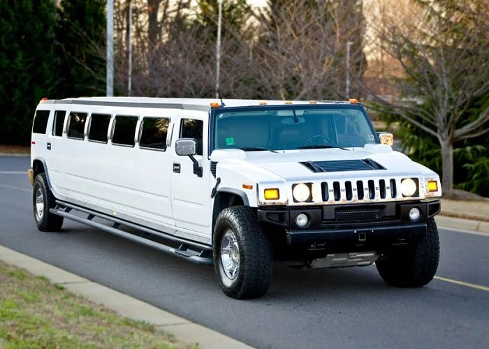 A white stretch limousine Hummer H2 parked on the side of a road.