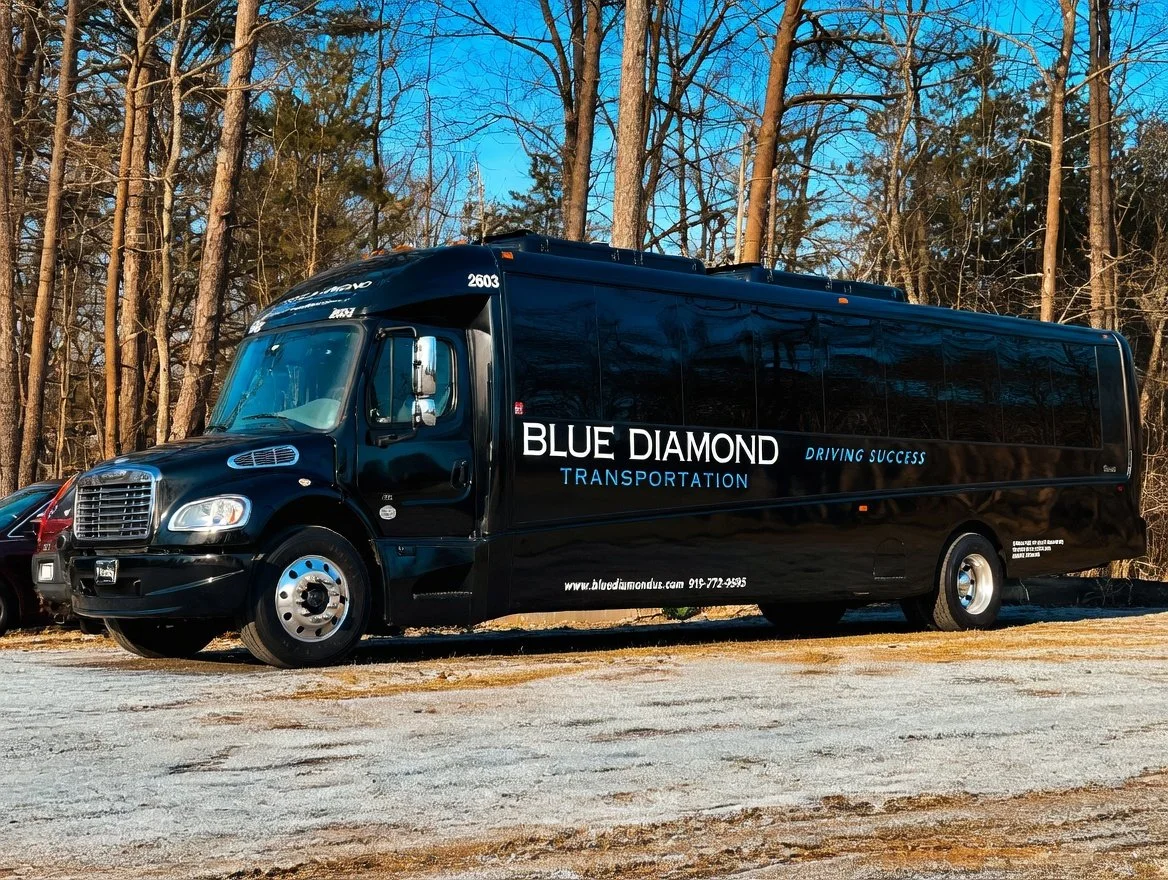 Black Blue Diamond Transportation Freightliner mini-bus parked on a gravel lot, with trees and a blue sky in the background.