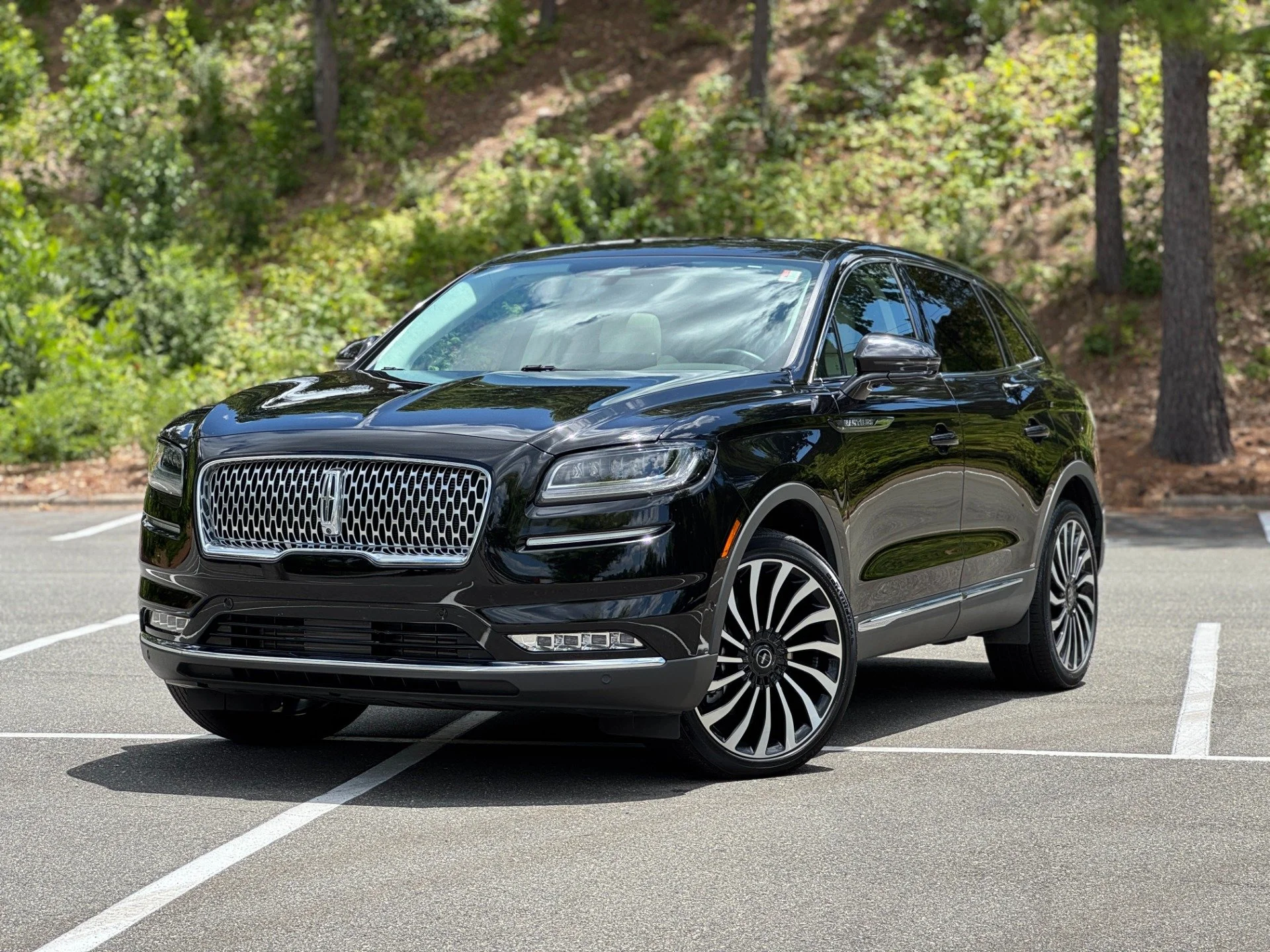 A shiny black Lincoln Nautilus SUV parked in an outdoor parking lot with trees and greenery in the background.