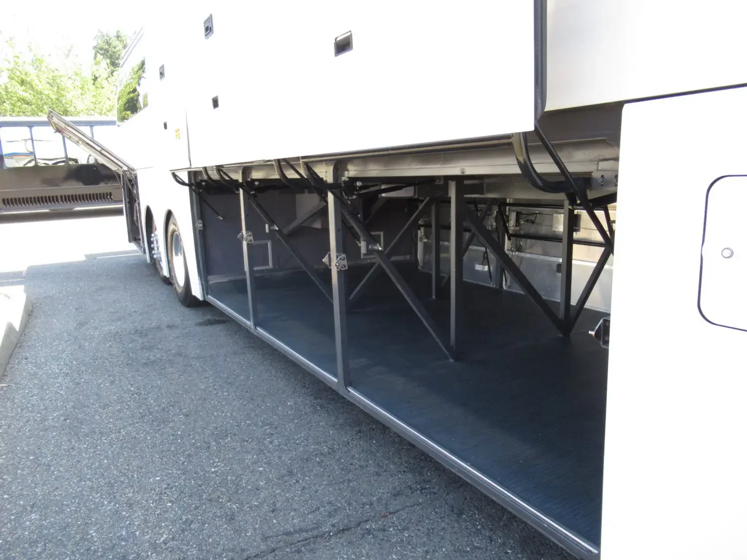 Open luggage compartment of a large white tour bus with black flooring and fold-out steps.