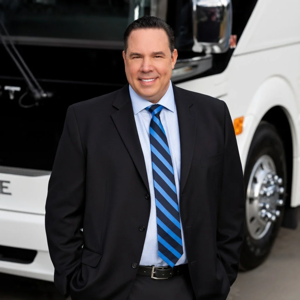 Gray Hill in business suit standing outdoors with one of his Blue Diamond Transportation buses.