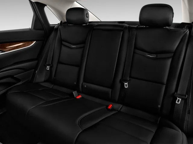Backseat interior of a car with black leather seats and seatbelts.