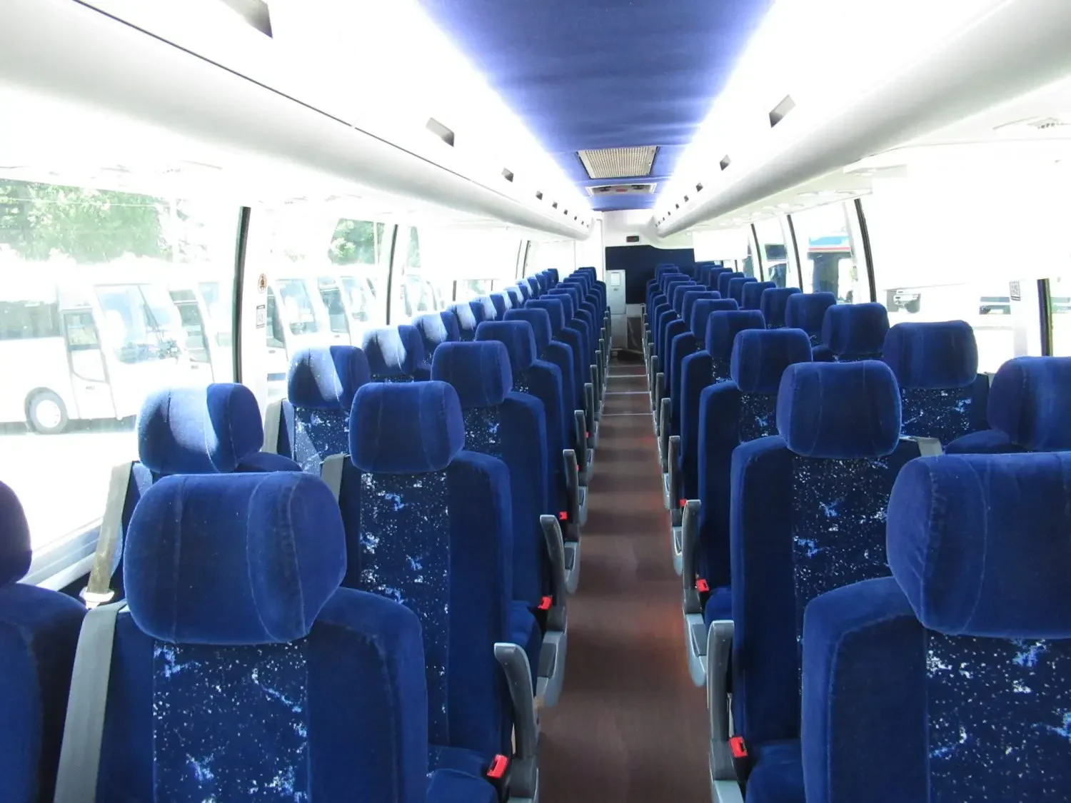 Interior of a bus with blue upholstered seats, clear windows on both sides, and a carpeted aisle.