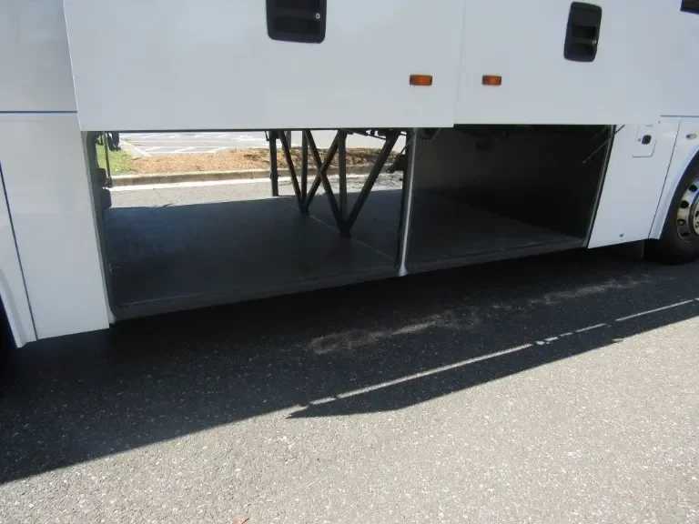 Empty luggage compartment of a white bus on a parking lot.