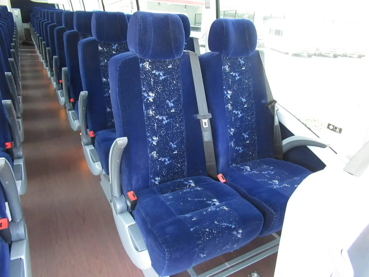 Empty blue upholstered airplane seats with headrests and seatbelts, arranged in rows inside an aircraft cabin.