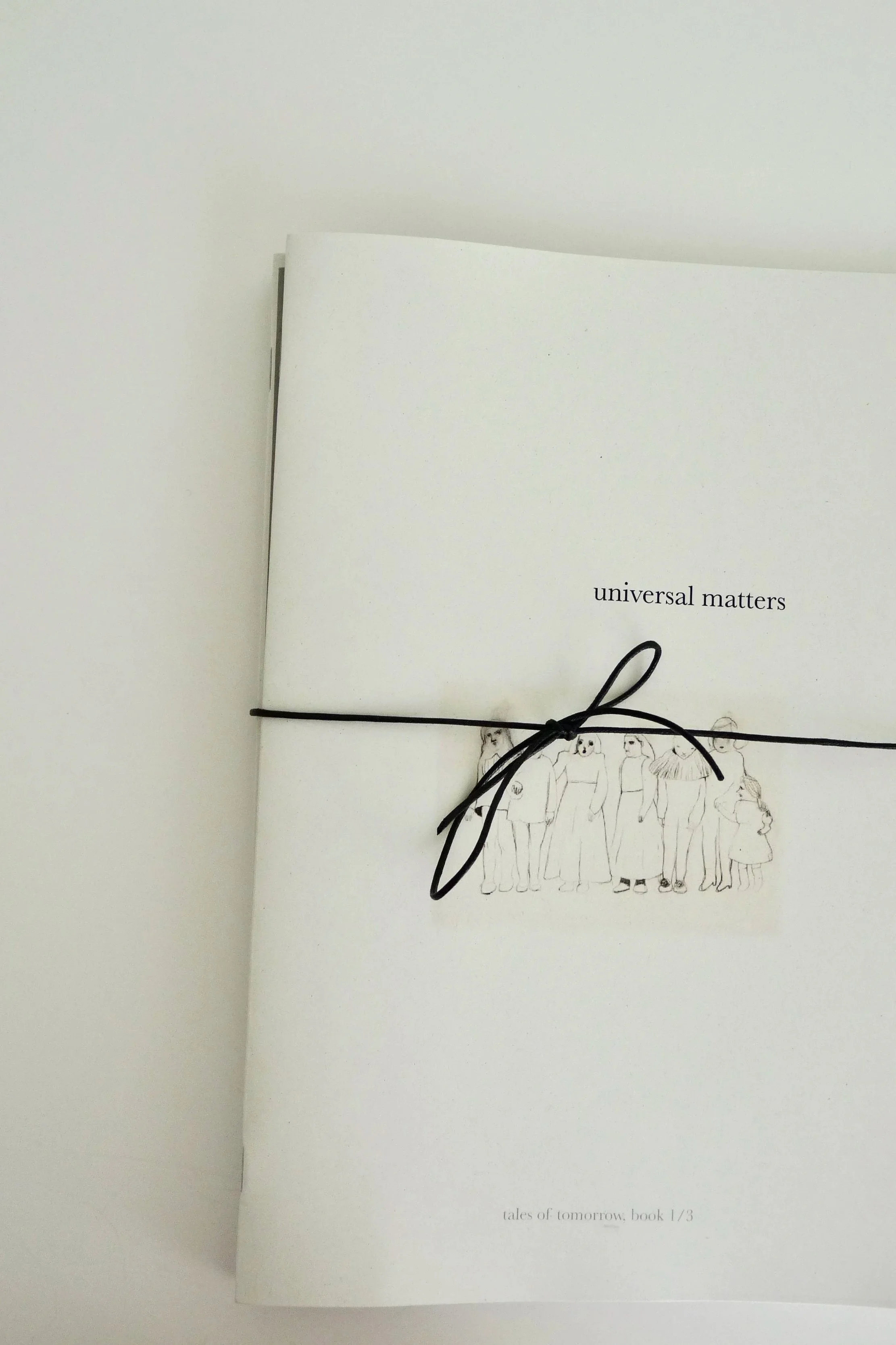 White booklet titled 'universal matters' tied with a black string, featuring an illustration of a group of people on the cover.