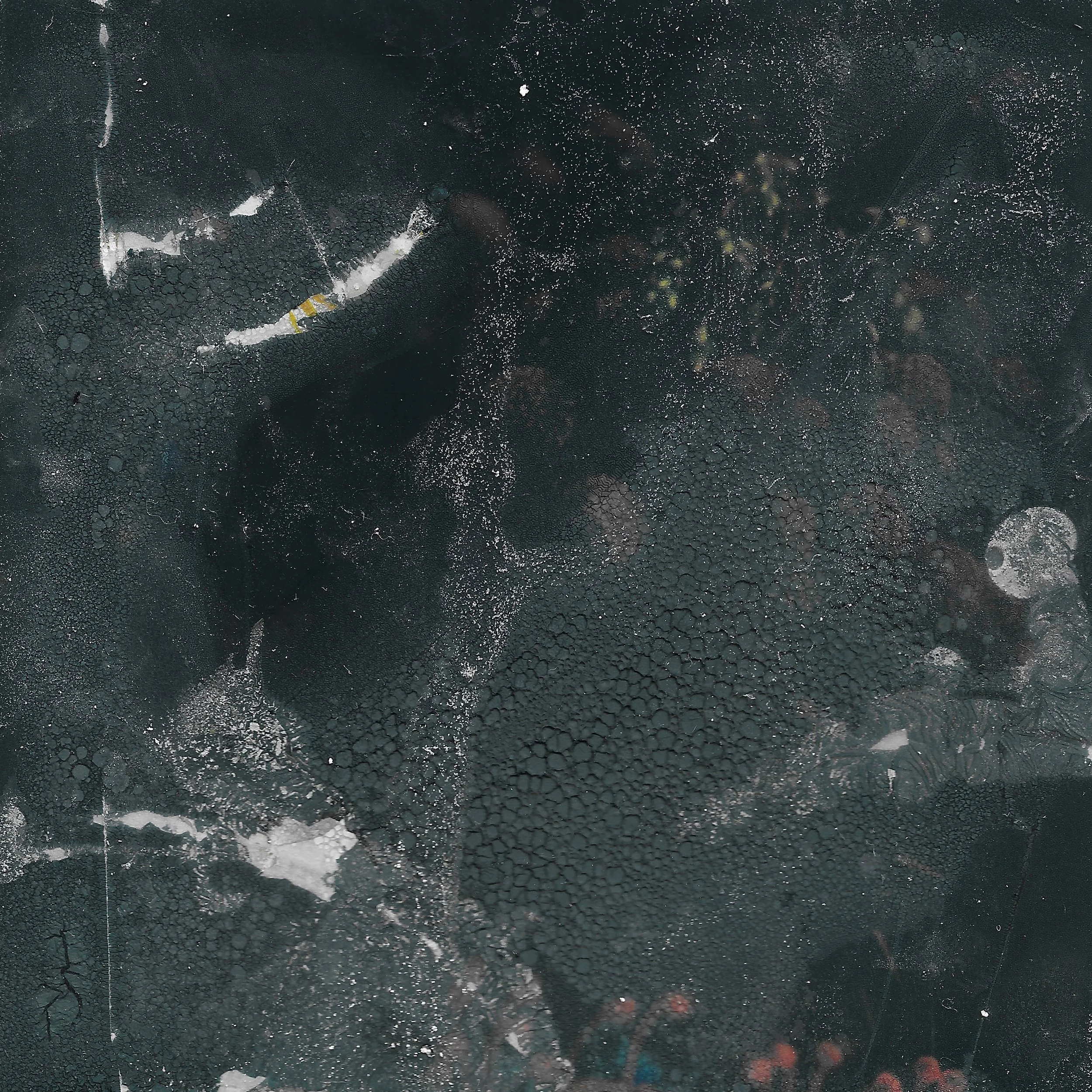 A close-up aerial view of a dark, cracked, and textured surface with patches of white and gray, possibly an outdoor terrain or asphalt.