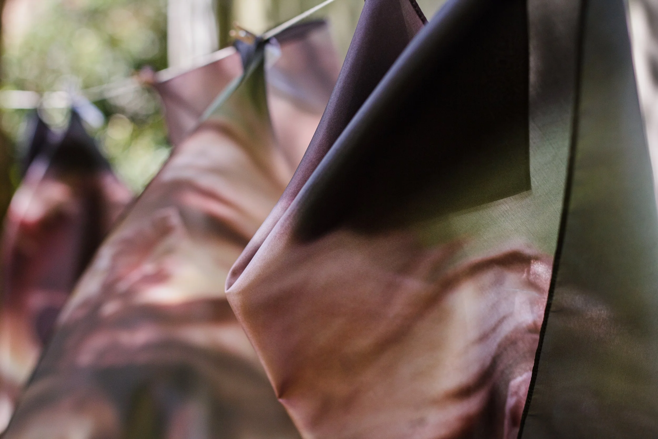 Close-up of several tote bags hanging outdoors with a nature background, featuring abstract and floral designs.