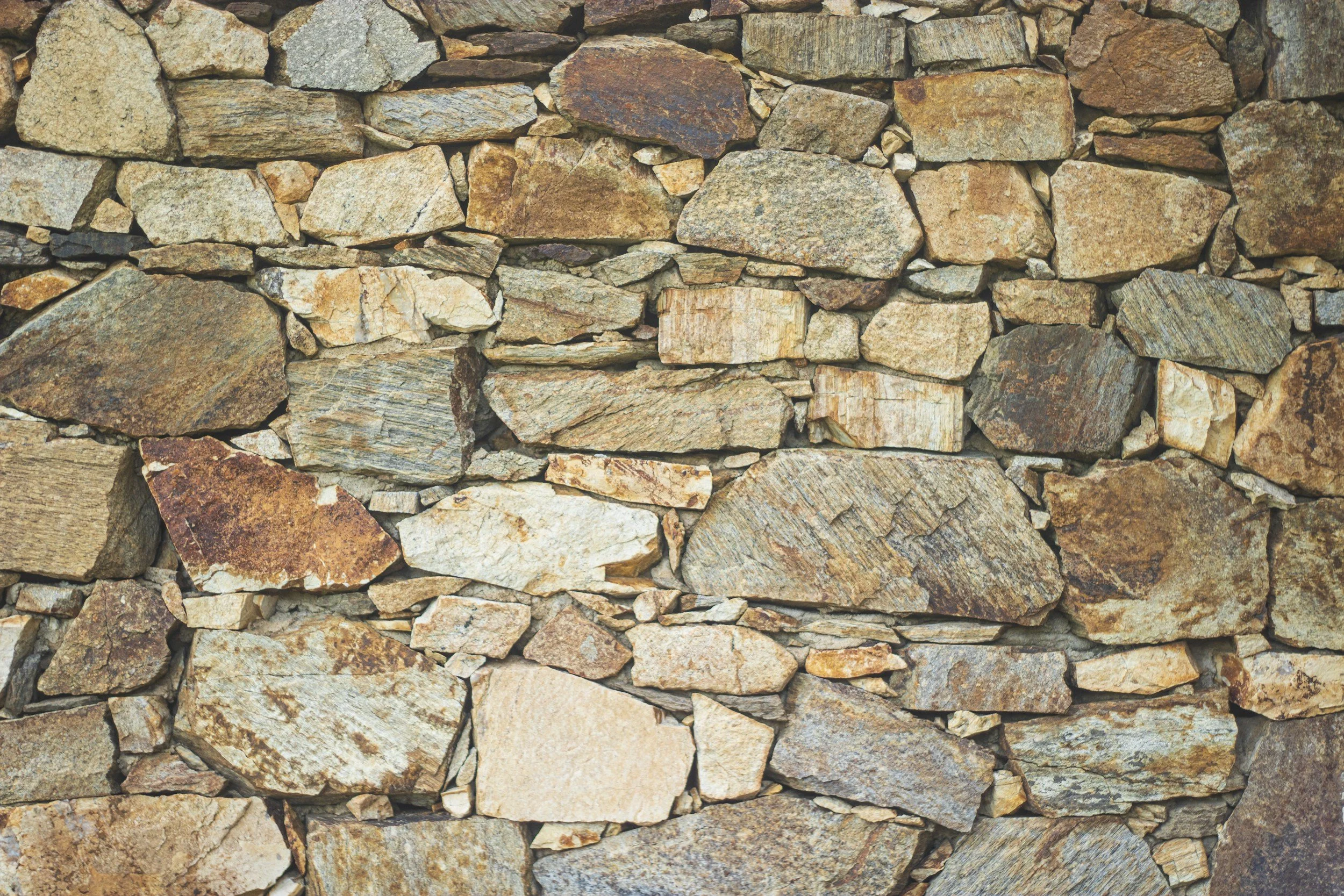 Close-up view of a dry stone wall made of irregularly shaped multicolored and textured stones stacked without mortar.