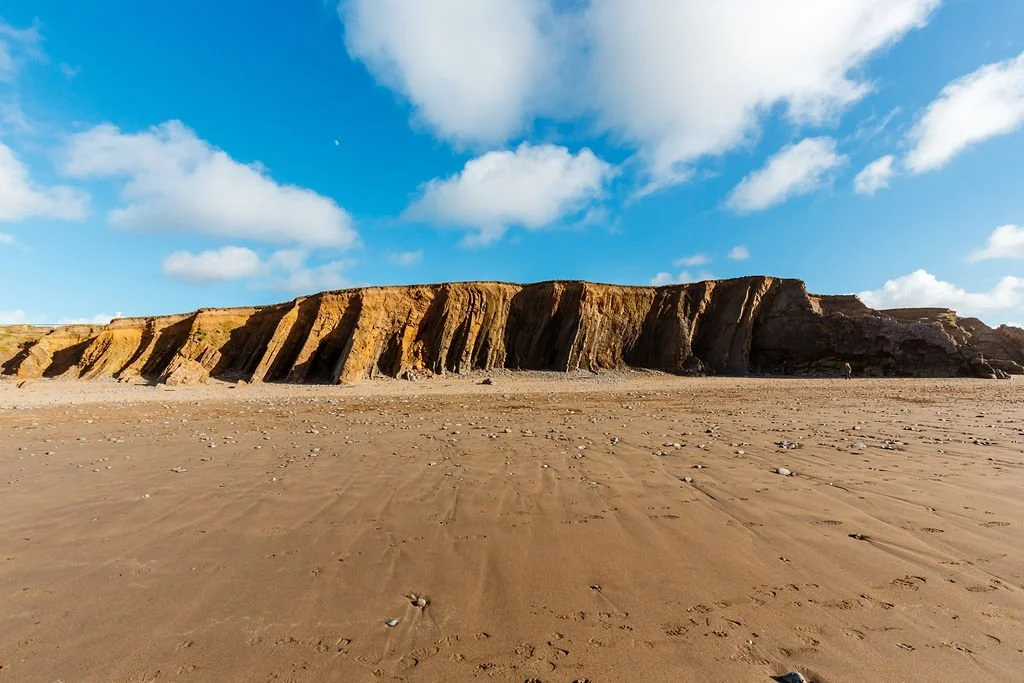 sandy beach with reddish cliffs under blue sky with scattered clouds