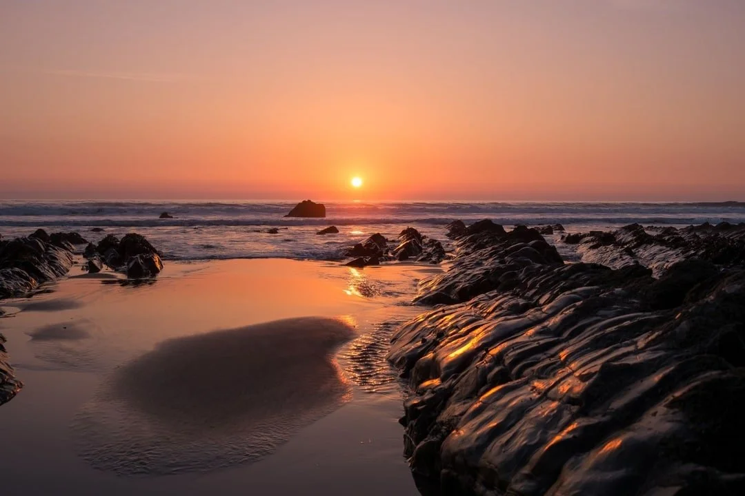 Sunset at the beach with rocks and tide pools reflecting the sky.