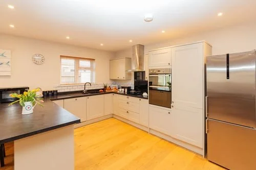 Modern kitchen with white cabinets, black countertops, stainless steel refrigerator, oven, and microwave, with a window and wooden floor.