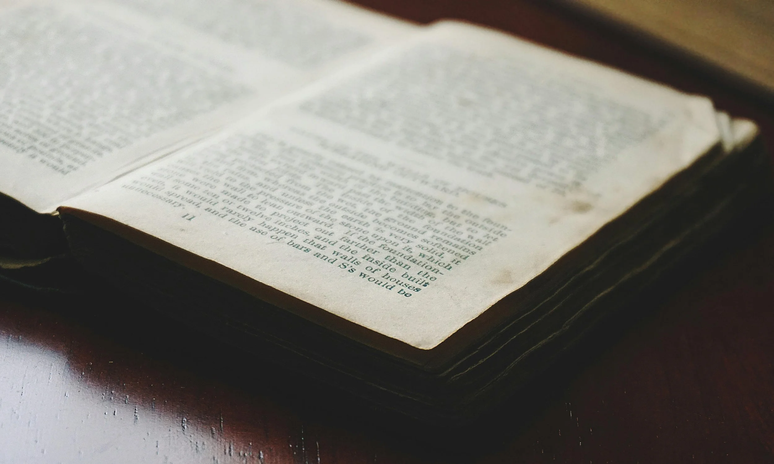 Close-up of an open book resting on a table, displaying pages with dense text.