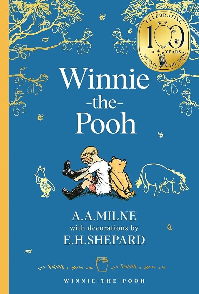 Cover of Winnie the Pooh book with blue background, featuring illustrations of Winnie the Pooh and Christopher Robin sitting together, surrounded by bees and tree branches, celebrating 100 years with a gold emblem in the top right corner.