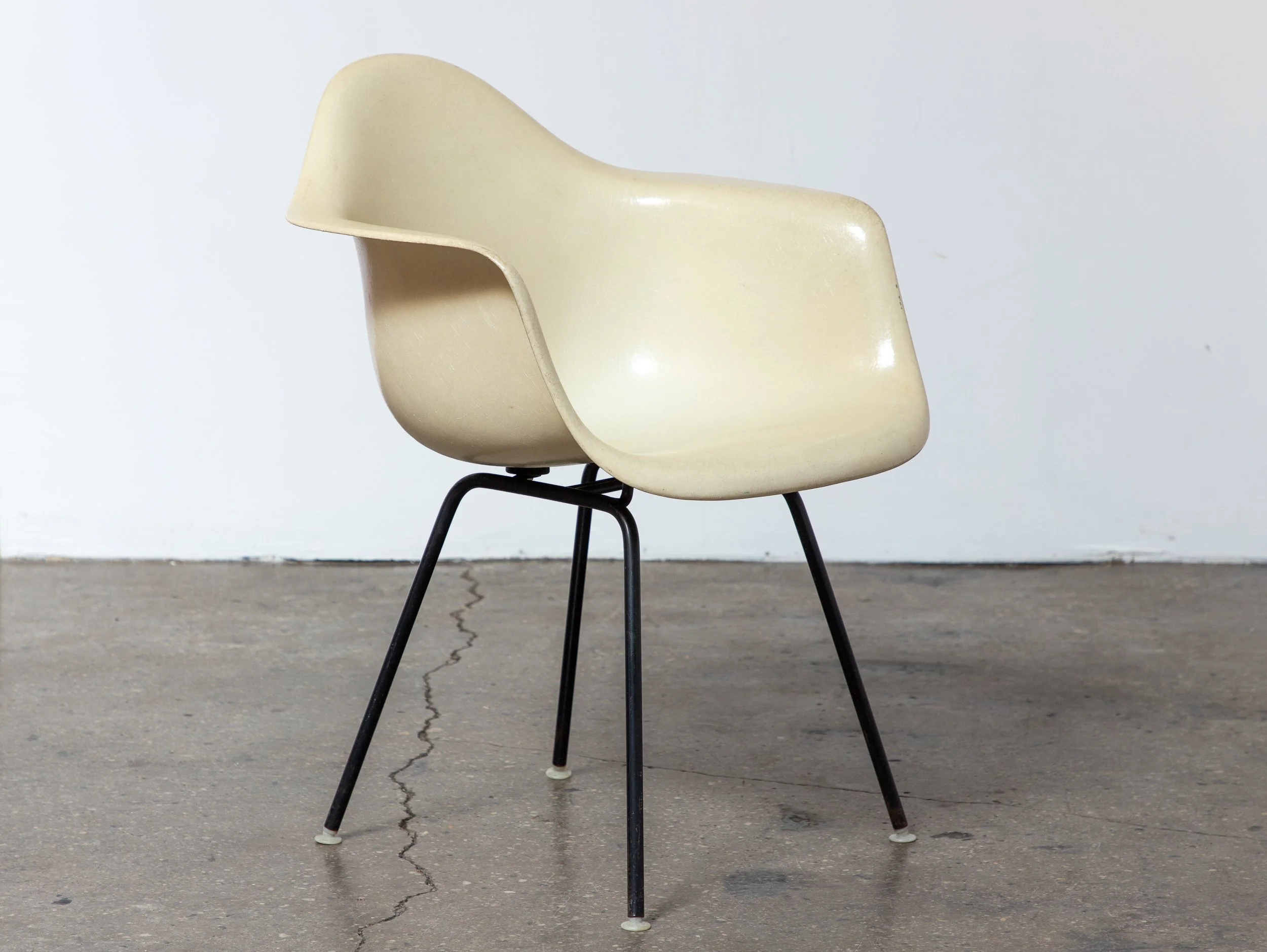 A vintage cream-colored fiberglass chair with metal legs is placed on a concrete floor against a plain light blue wall.