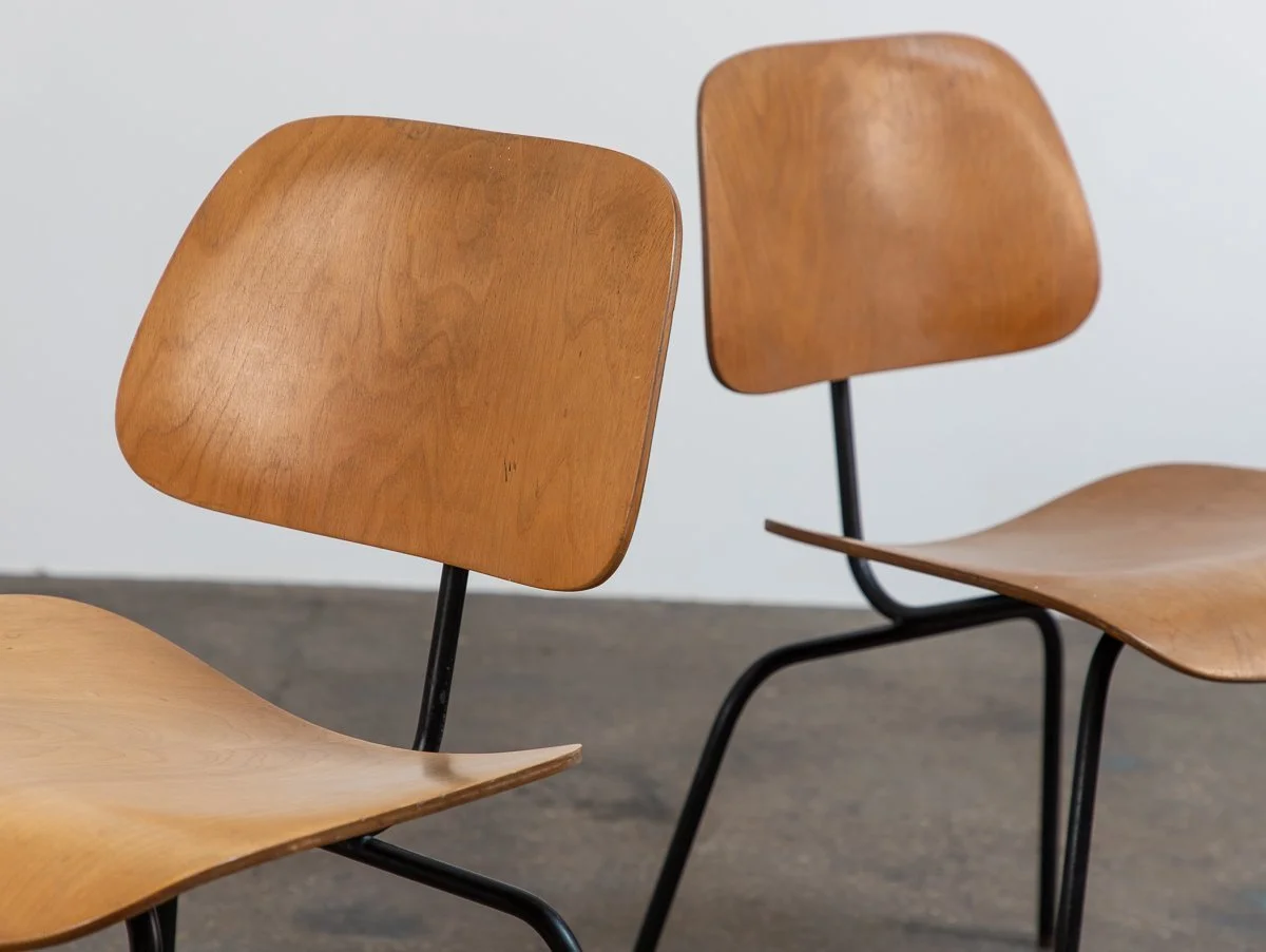 Two wooden chairs with curved seats and backs, supported by black metal legs, placed on a gray floor against a plain white background.