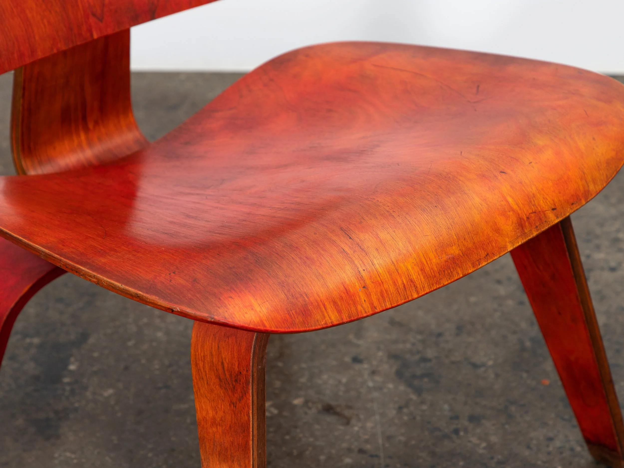 Close-up of a curved wooden chair with reddish stain and visible wood grain.