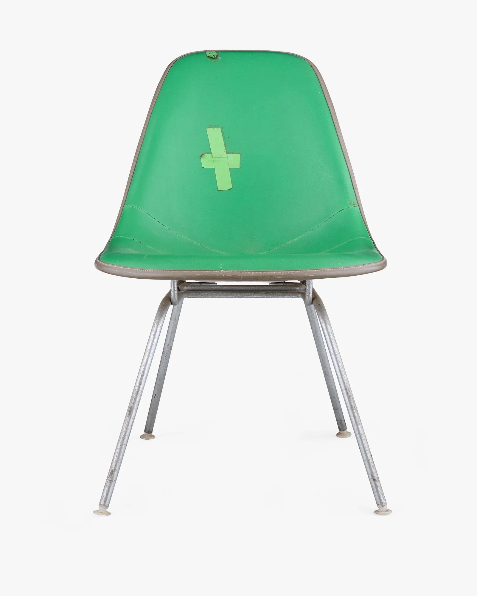 Green vintage chair with a white cross taped on the backrest, metal legs, and a white background.