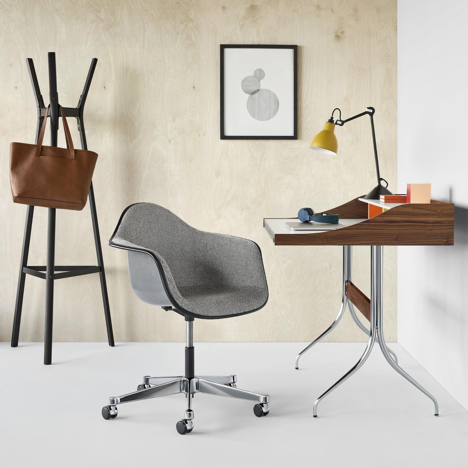 A modern workspace with a black office chair, a wooden desk, a yellow desk lamp, a framed artwork of three gray circles, a wall with beige and white sections, a gray mesh chair, a blue wireless headset, and a stack of books.
