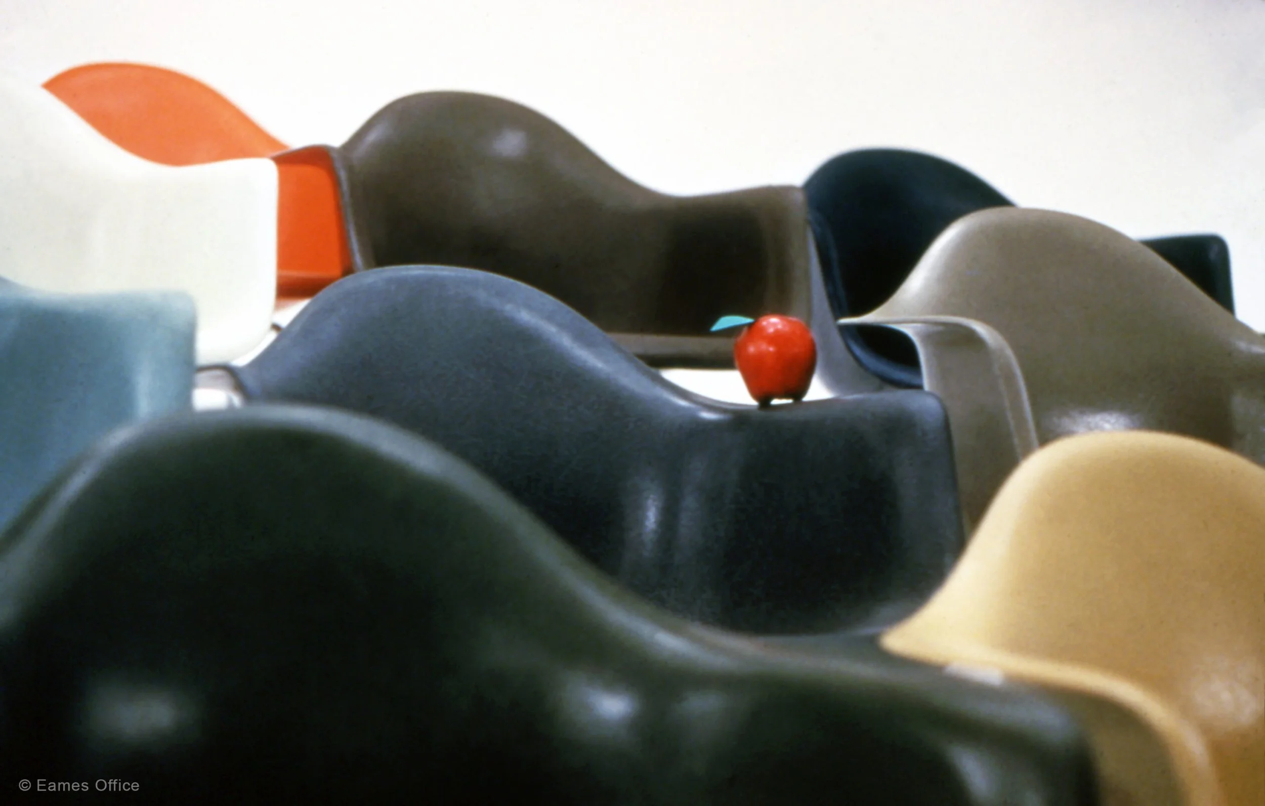 Multiple colorful toy animal figurines arranged on a surface, including a red apple-shaped figure in the foreground.