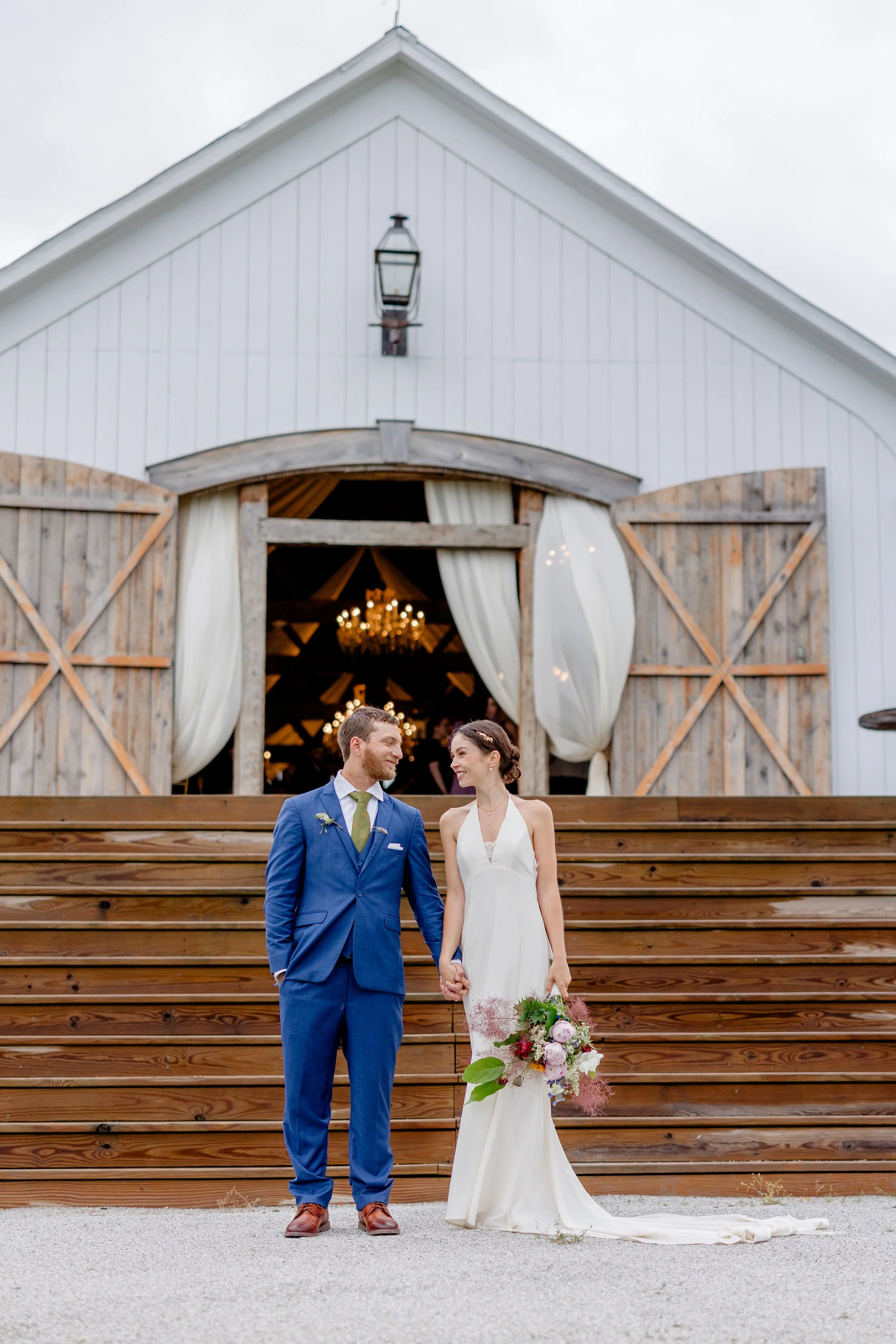 Newlywed couple standing at the bottom of the chapel‑style steps with the Wedding Barn doors open at Swiss & Bloom Farm.