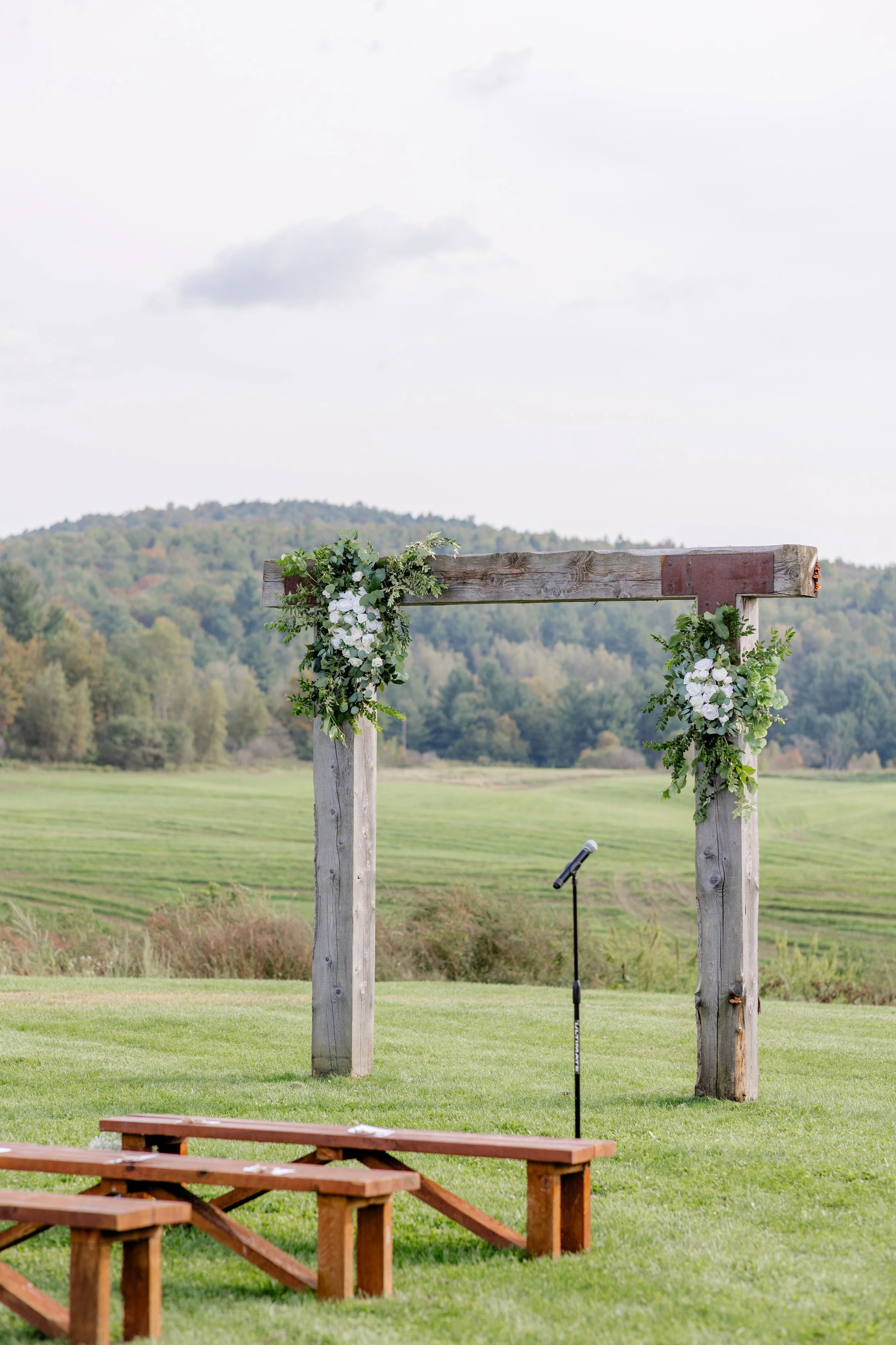 Floral‑adorned wooden ceremony arch set against open fields at Swiss & Bloom Farm.