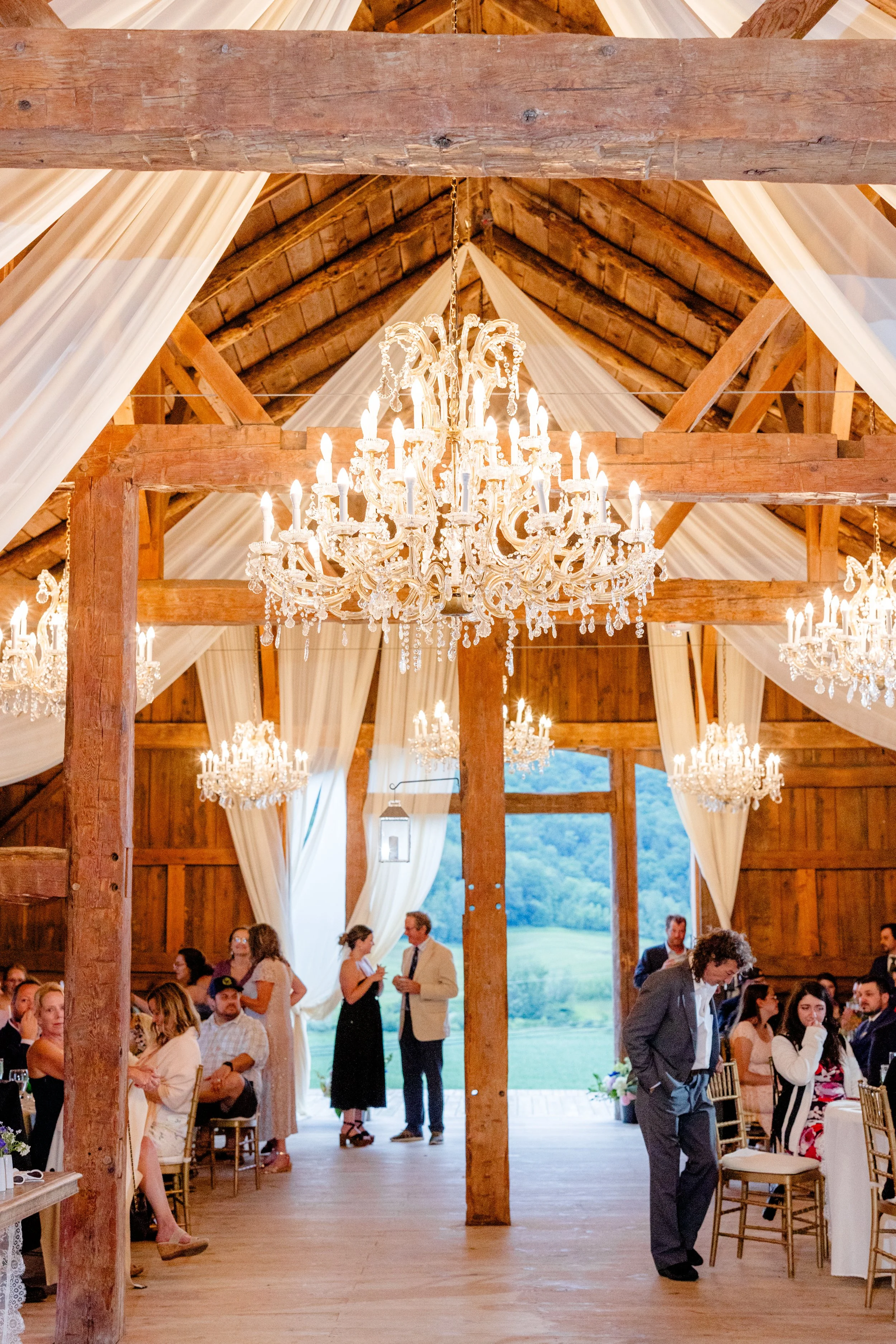 Elegant Wedding Barn interior with chandeliers, soft draping, and restored whitewashed beams at Swiss & Bloom Farm.