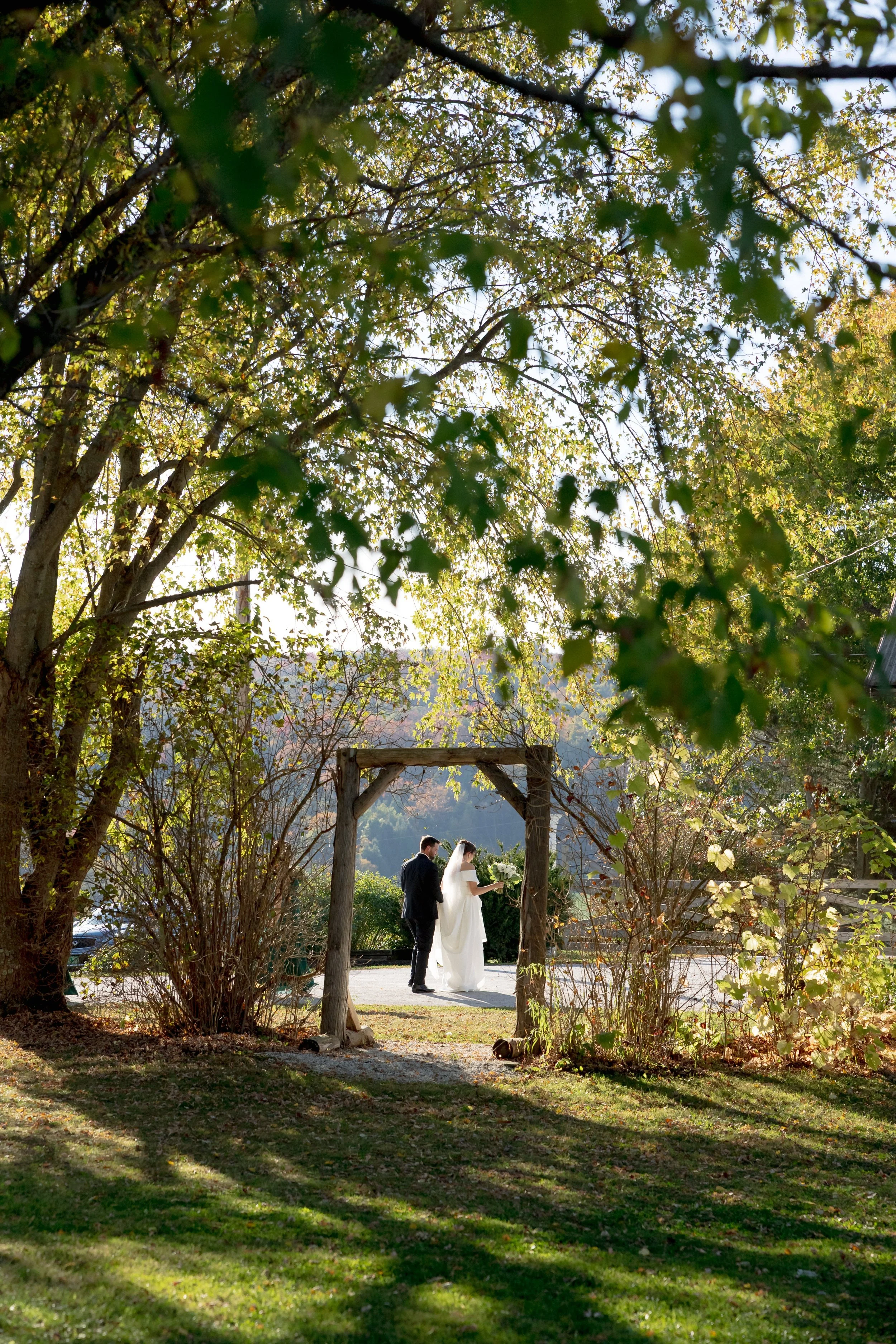 Bride and groom walking beneath a handcrafted wooden archway surrounded by Vermont woodland at Swiss & Bloom Farm.