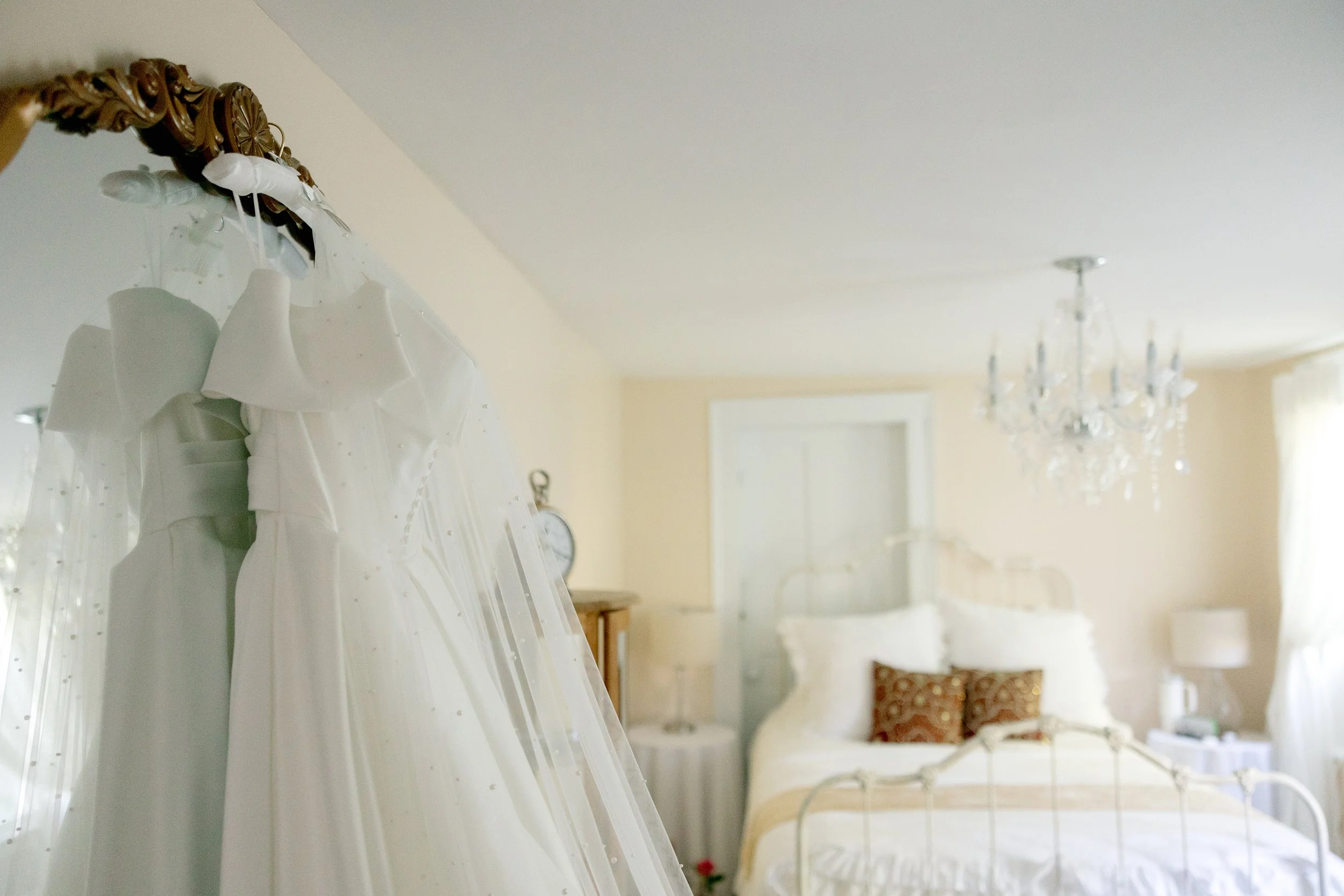 Elegant bridal suite with chandelier lighting and a wedding dress hanging beside the bed at Swiss & Bloom Farm.