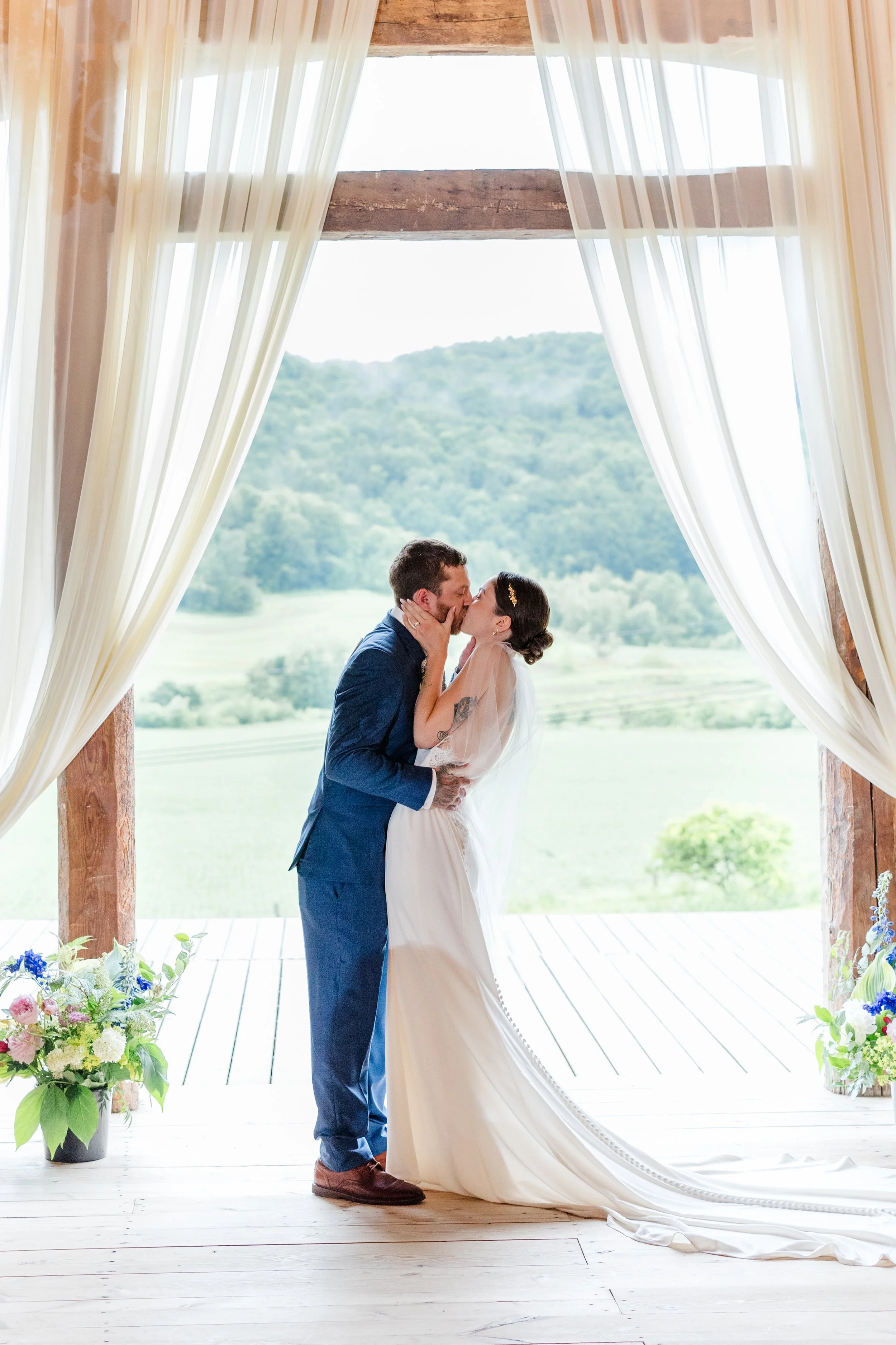Bride and groom sharing a kiss inside the rustic wooden ceremony alcove draped in soft fabric at Swiss & Bloom Farm.