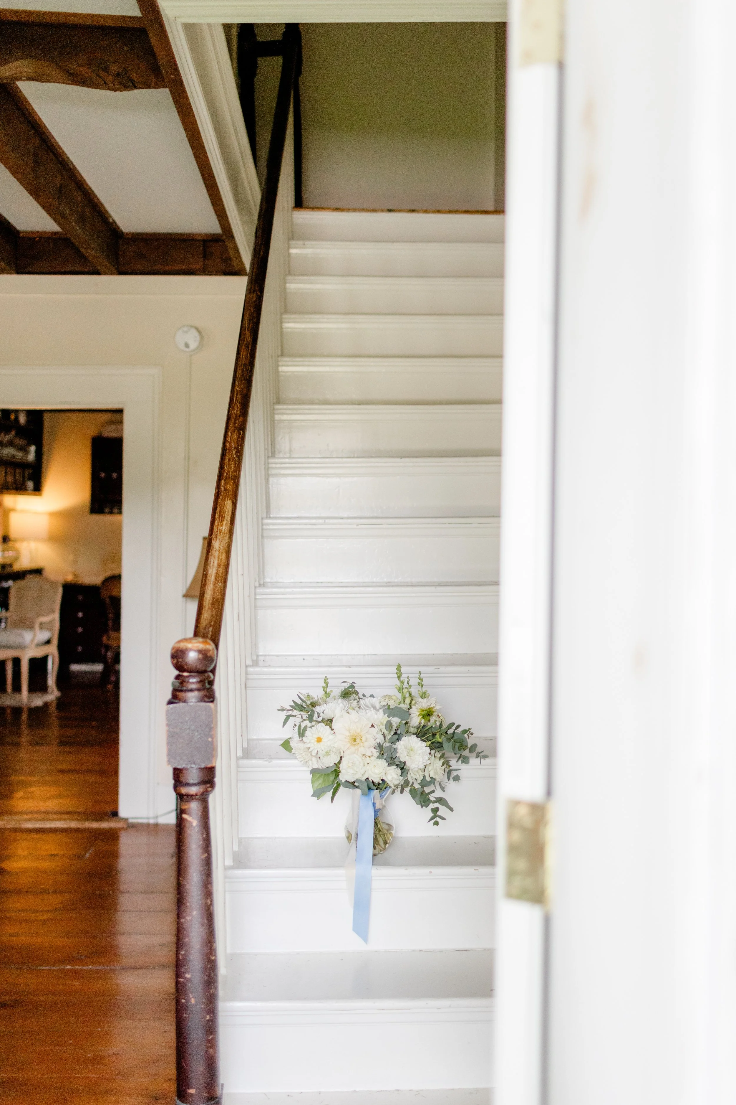 Open wooden staircase inside the Farmhouse at Swiss & Bloom Farm with natural light and white walls.