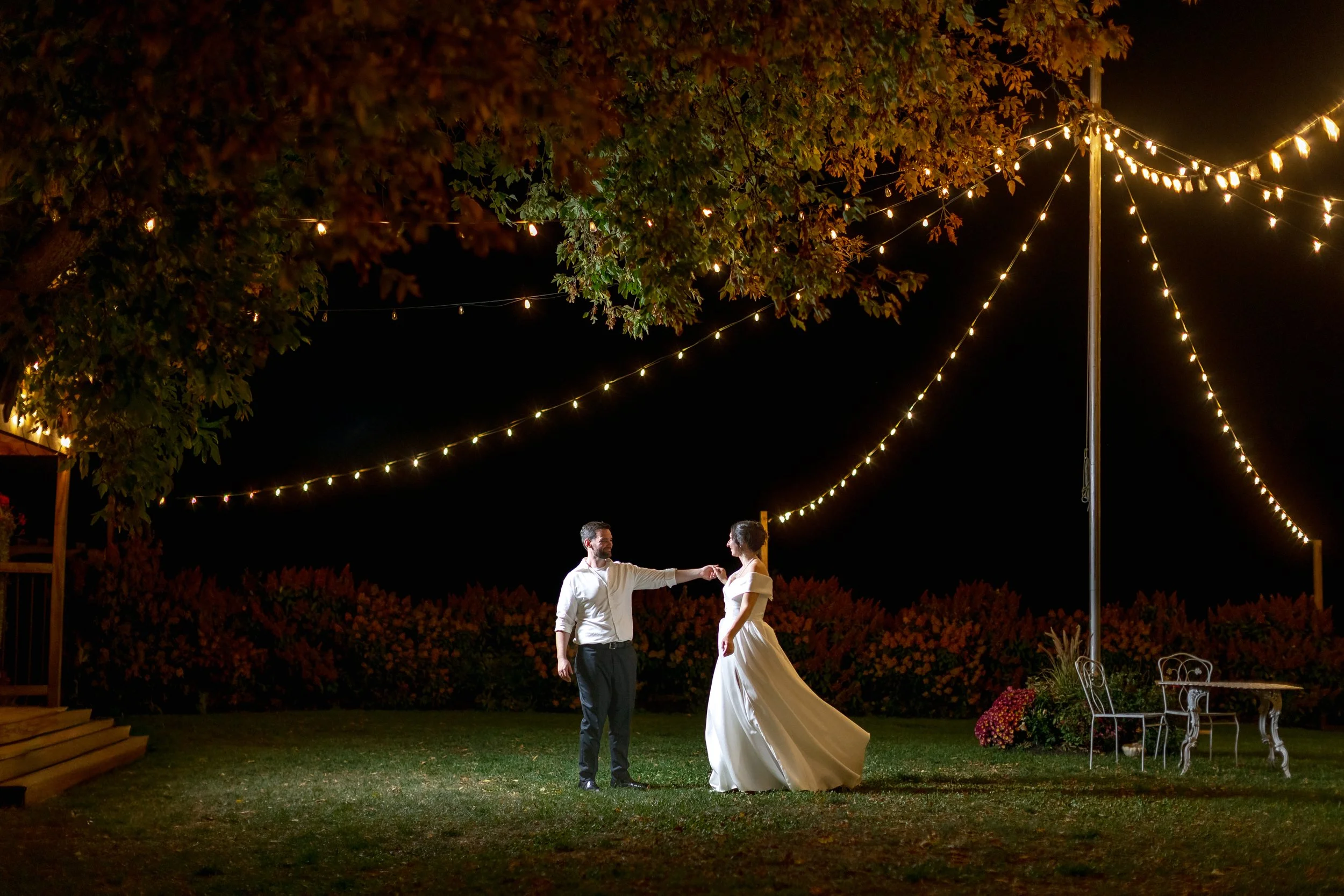 Bride and groom dancing under string lights outside the Wedding Barn during a Vermont summer evening celebration.
