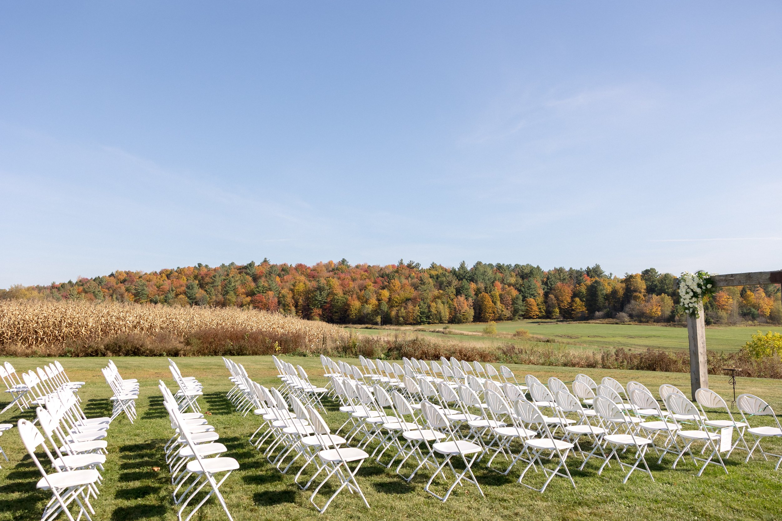 White ceremony chairs arranged on the lawn overlooking the Vermont hillside at Swiss & Bloom Farm.