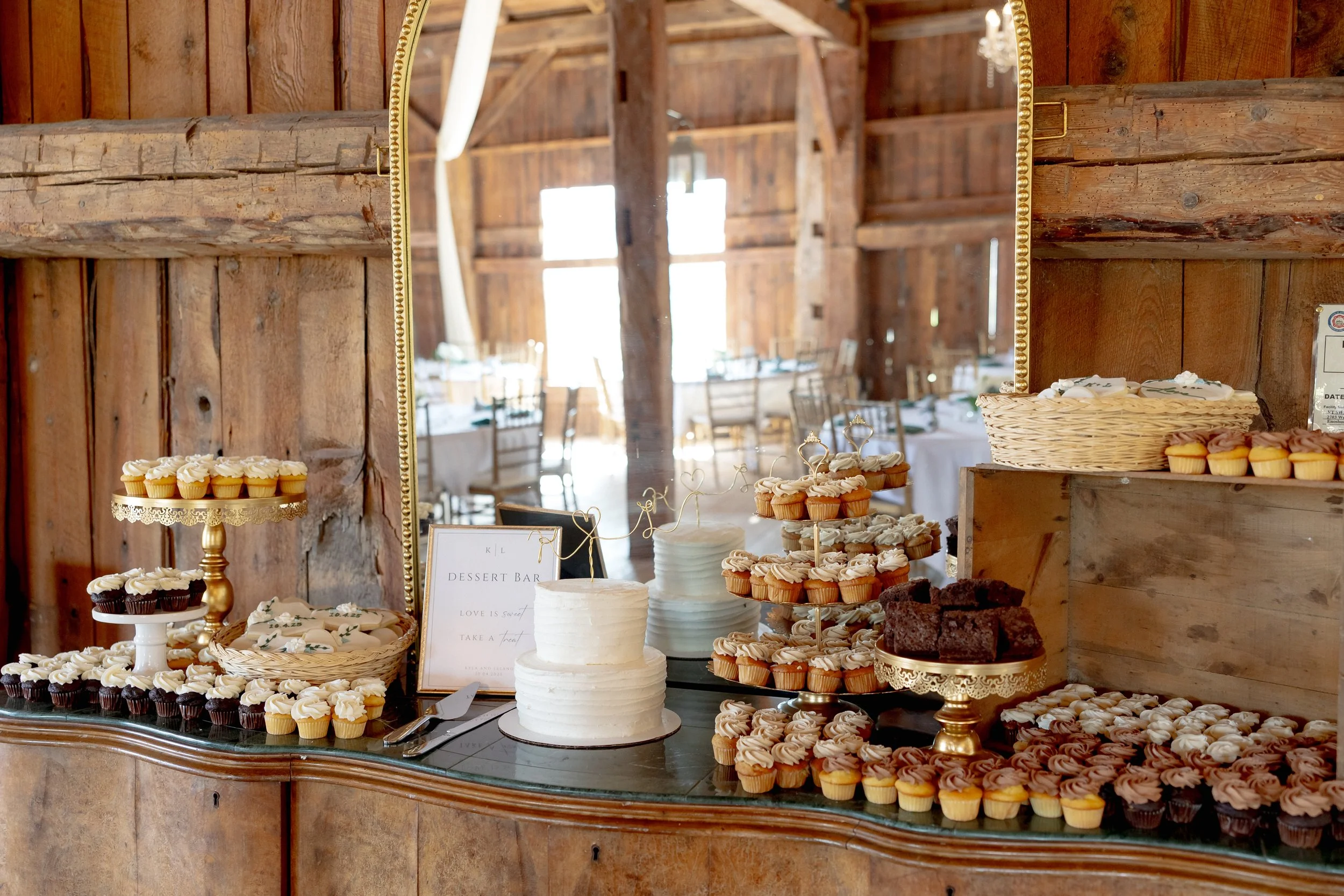 Wedding dessert table with a tiered cake and cupcakes displayed inside the Wedding Barn at Swiss & Bloom Farm.