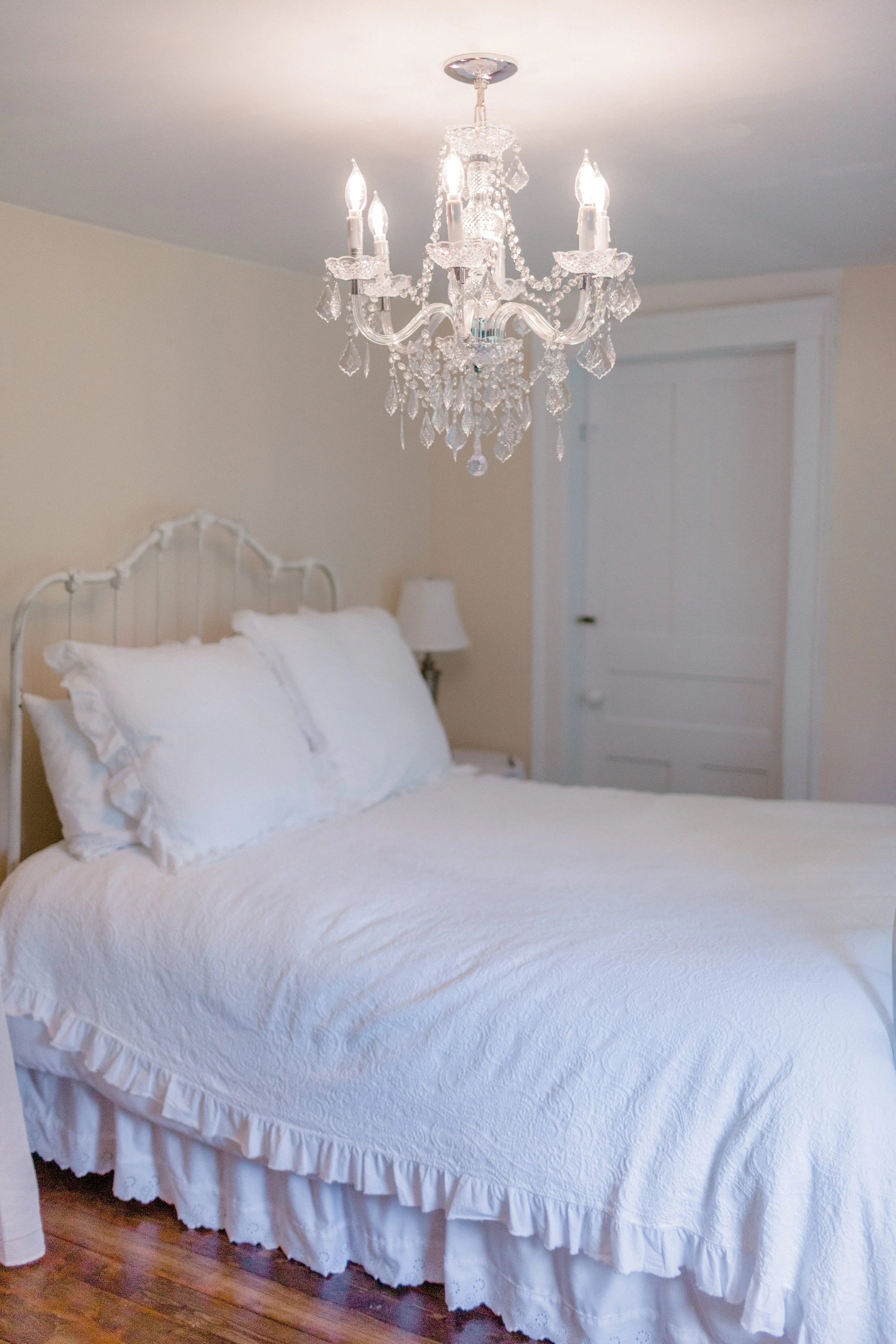 Farmhouse bedroom at Swiss & Bloom Farm with an antique bed, chandelier, and soft natural light.