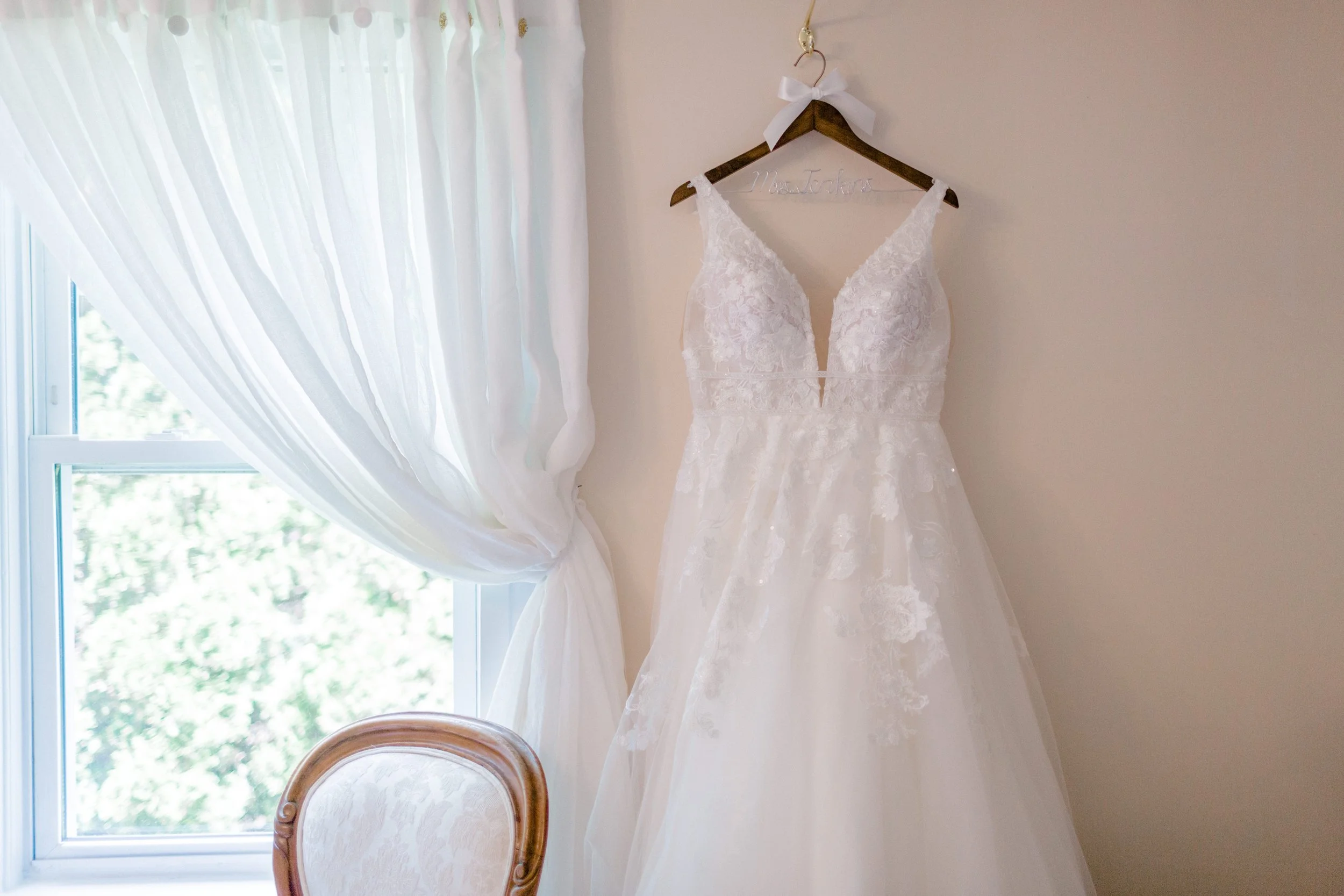 Bedroom inside the Farmhouse at Swiss & Bloom Farm with a wedding dress hanging near the window and antique furnishings.