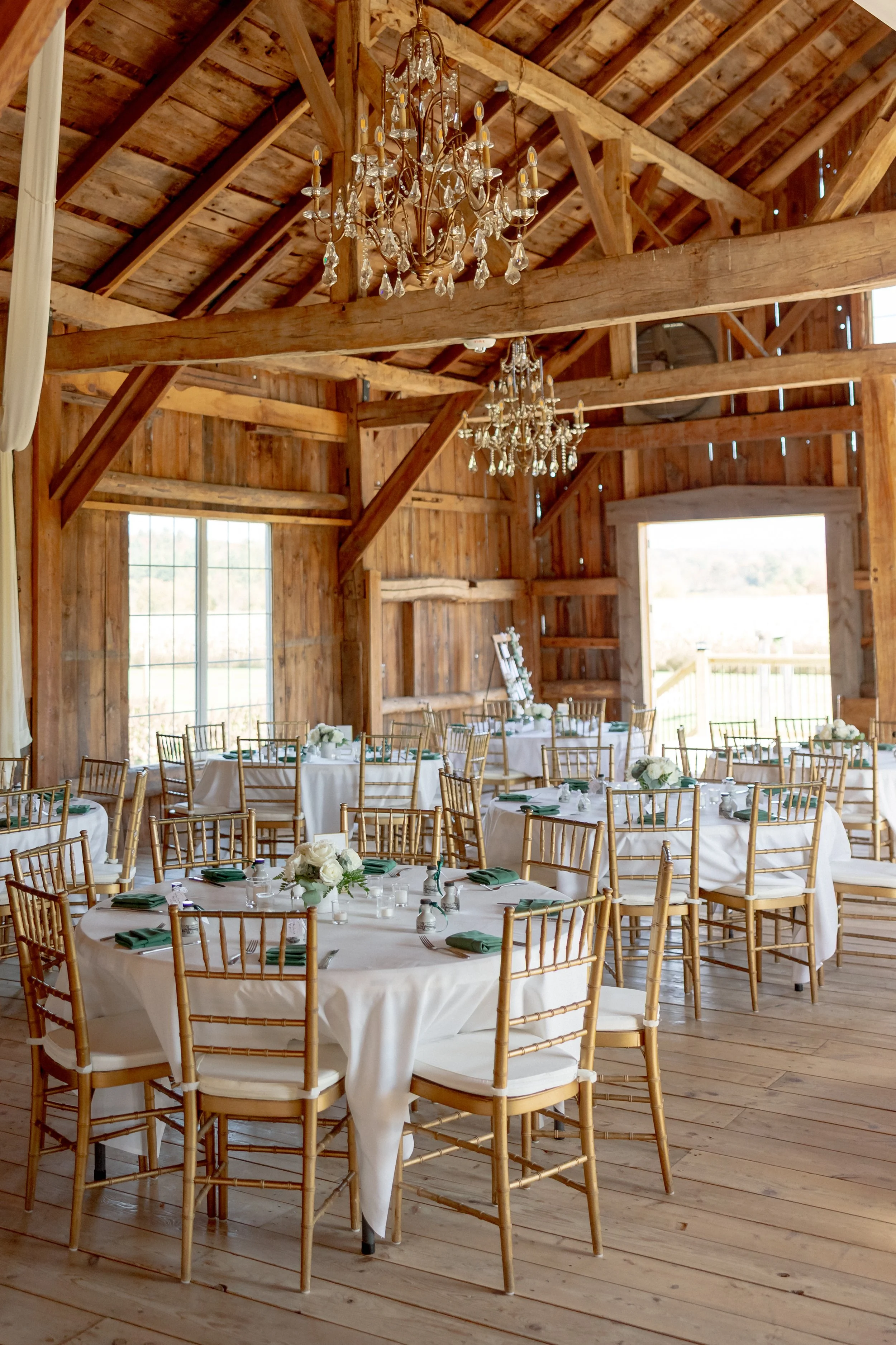 Elegant Wedding Barn reception setup with chandeliers, round tables, and gold chairs at Swiss & Bloom Farm.