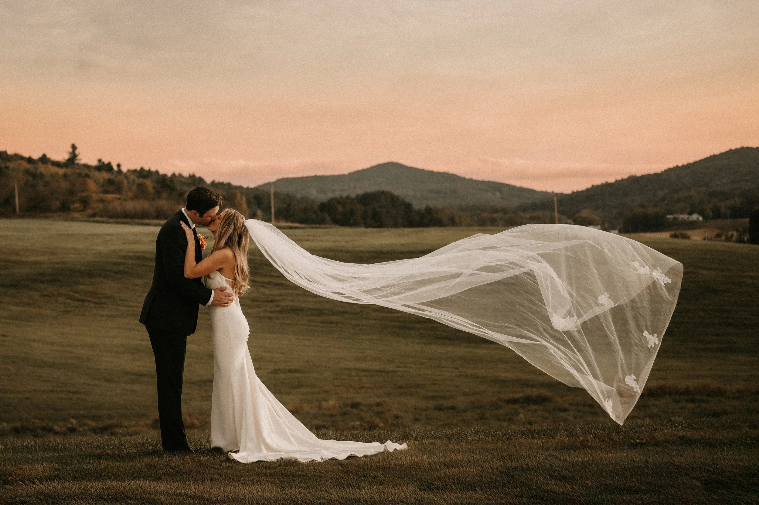 Bride and groom embracing in an open field at Swiss & Bloom Farm with rolling Vermont hills and sunset light.