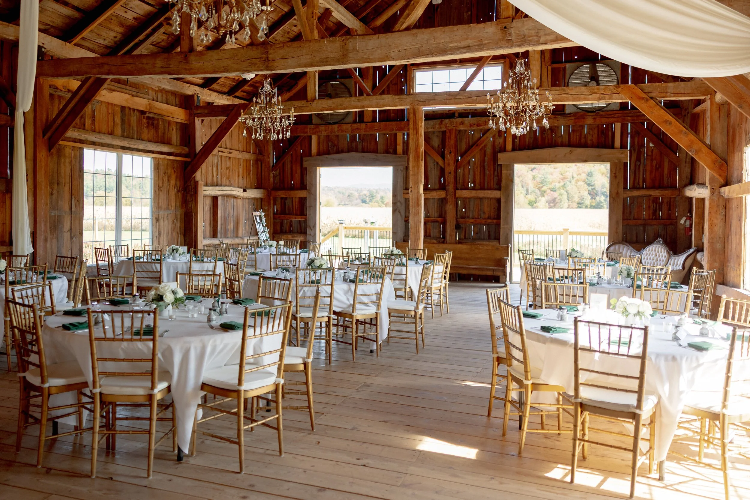 Wedding reception tables inside the Wedding Barn at Swiss & Bloom Farm with white linens, gold chairs, and floral centerpieces.