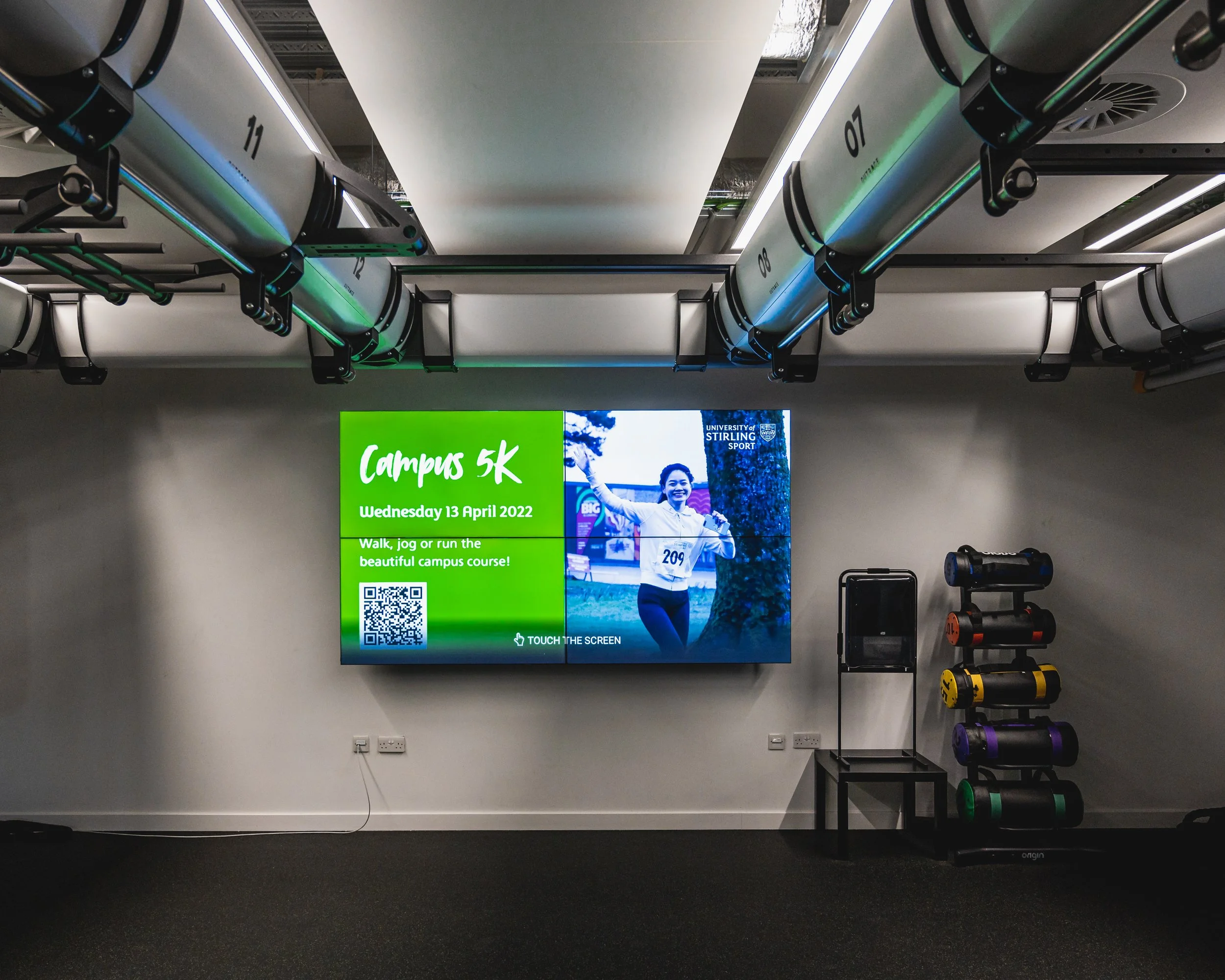 Digital sign display promoting a campus 5K event at the University of Stirling, with a picture of a smiling woman running and details about the event happening on Wednesday, April 13, 2022.
