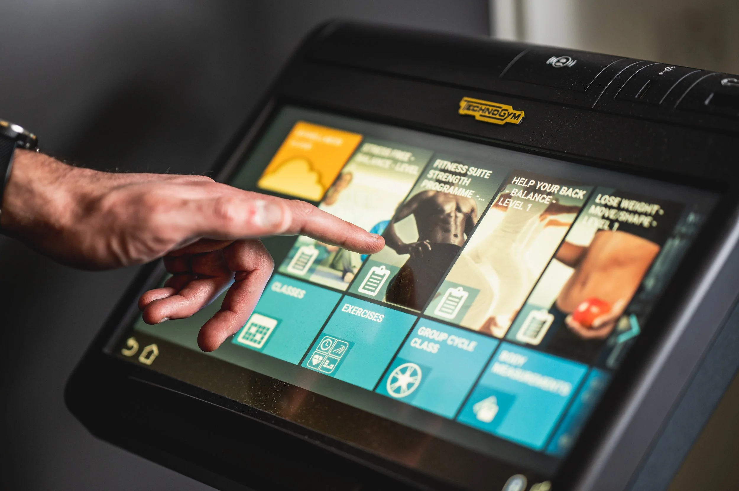 Person touching a touchscreen interface displaying workout program options at Technogym.
