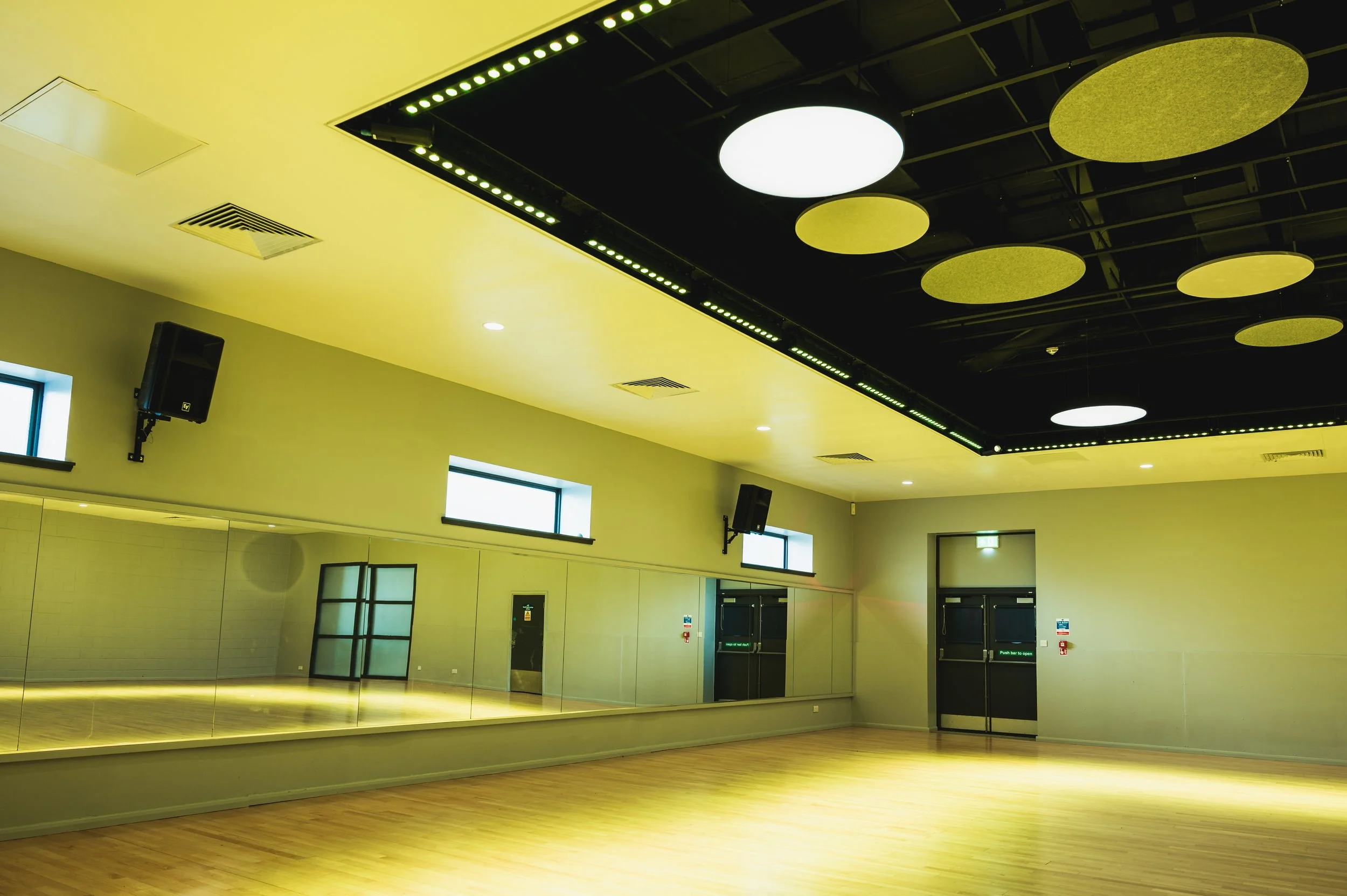 An empty dance studio with a yellow ceiling, a mirror wall, and ceiling-mounted large round yellow and white acoustic panels.
