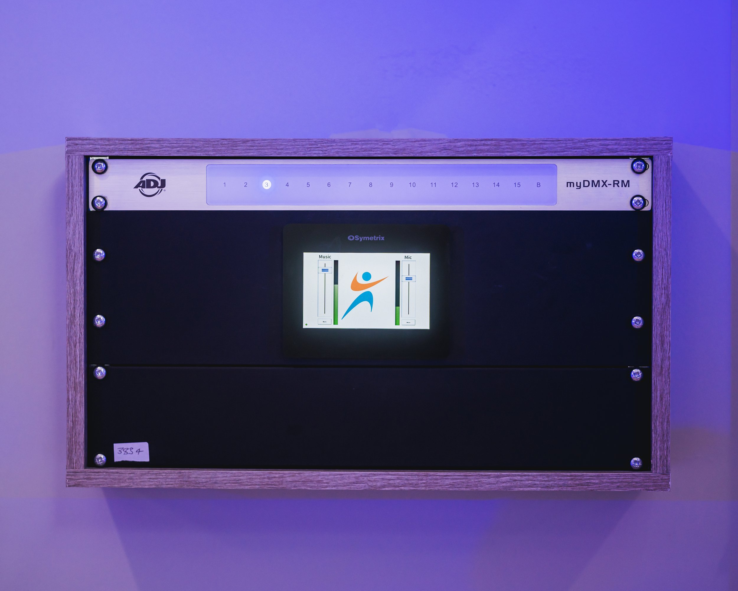 Close-up of a wooden-framed display with a panel showing an ADJ logo, printed numbers from 1 to 15 and B, and a digital screen with colorful graphics and controls.