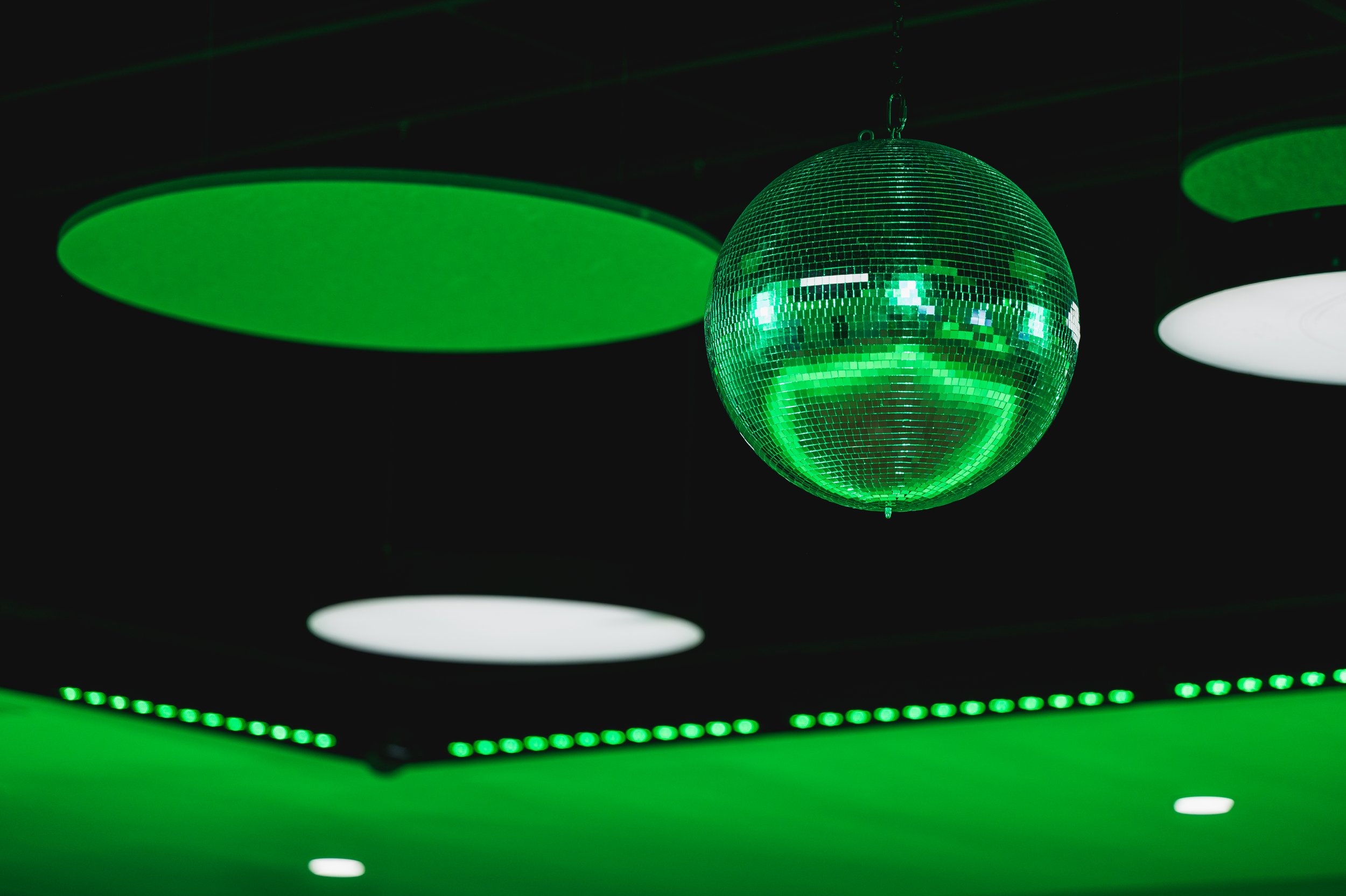 Green disco ball hanging from the ceiling with green and white circular light fixtures nearby.